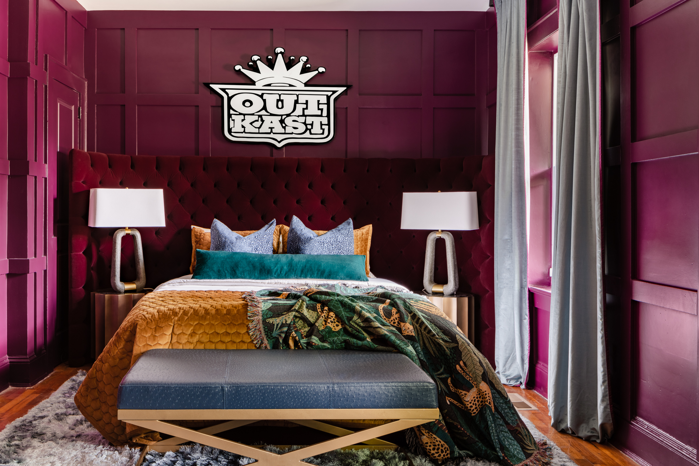 The Dungeon House bedroom with purple walls and Outkast plaque above colorful bed