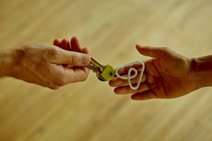 Una mano entrega llaves con llavero de logo de Airbnb en color blanco a otra mano que está extendida