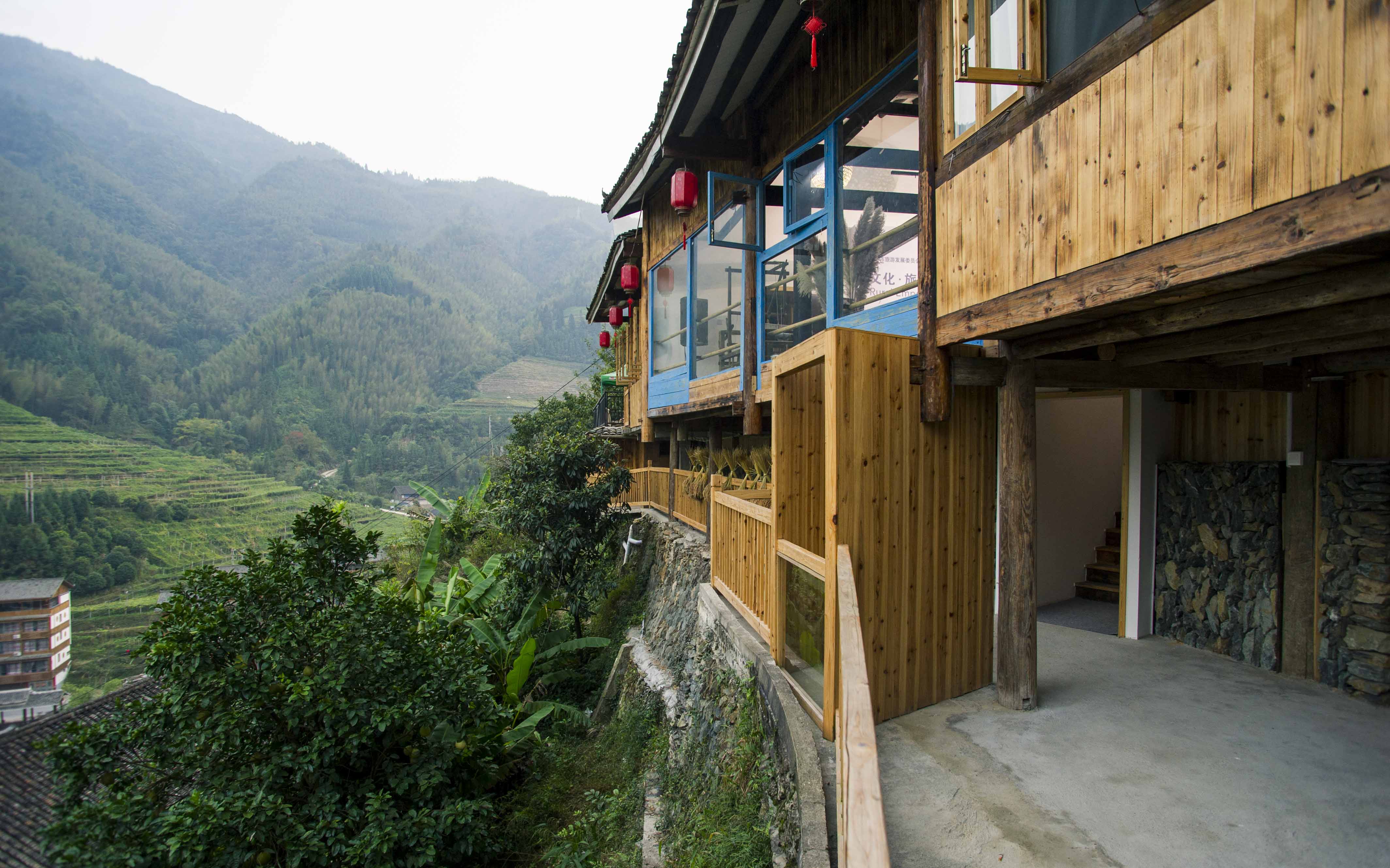 A wooden house overlooks a foggy valley in the mountains of Guilin.