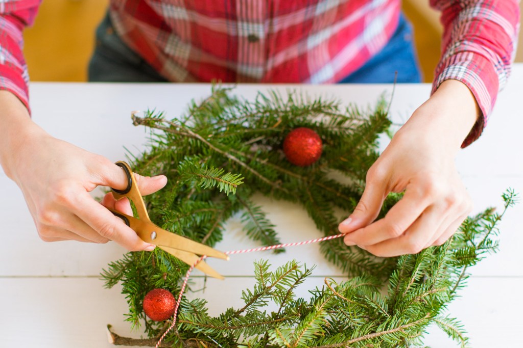 A woman's hands cutting string to decorate a Christmas wreath.