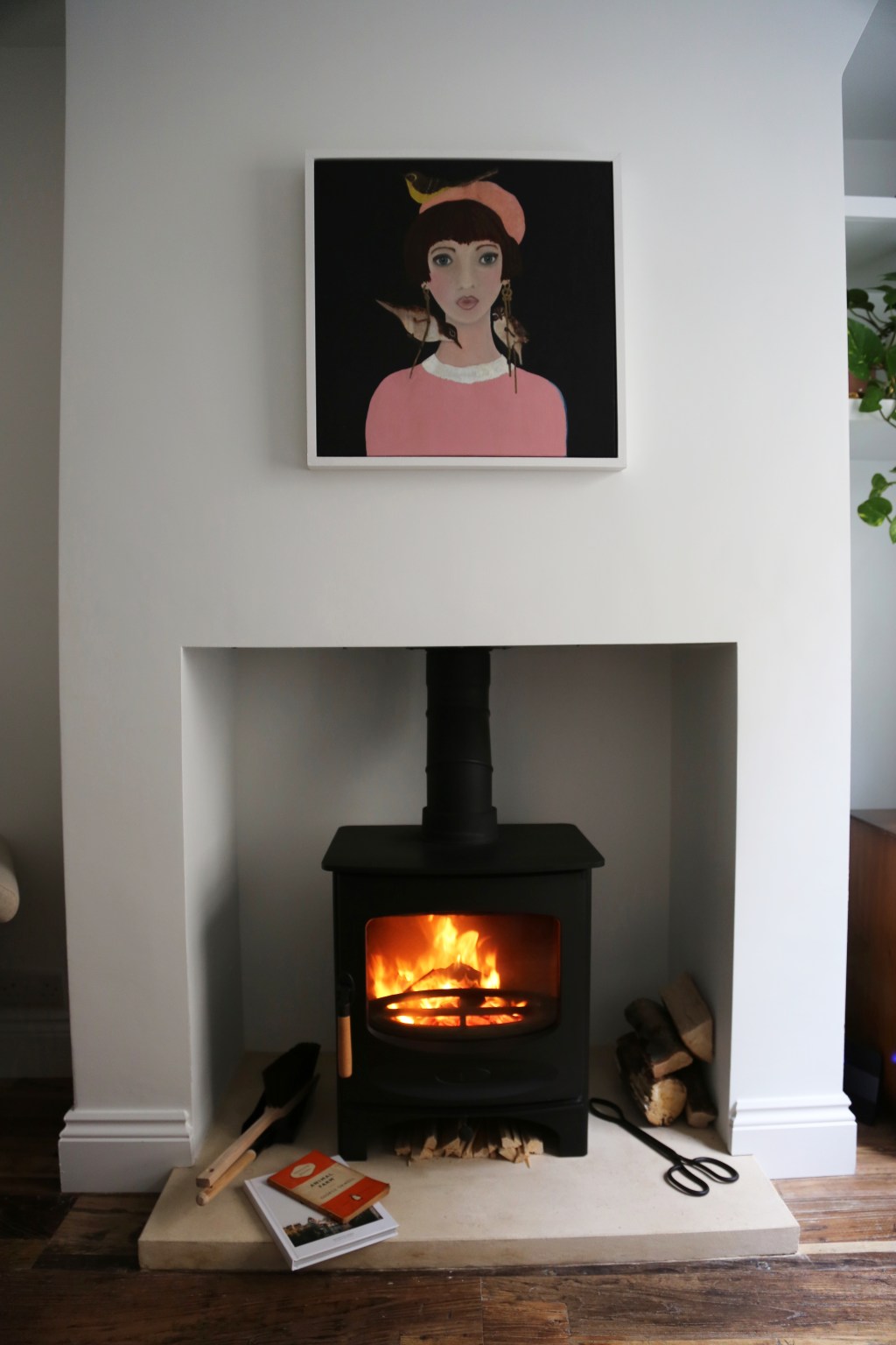 Lit fireplace with a portrait painting of a woman in a pink shirt and hat.