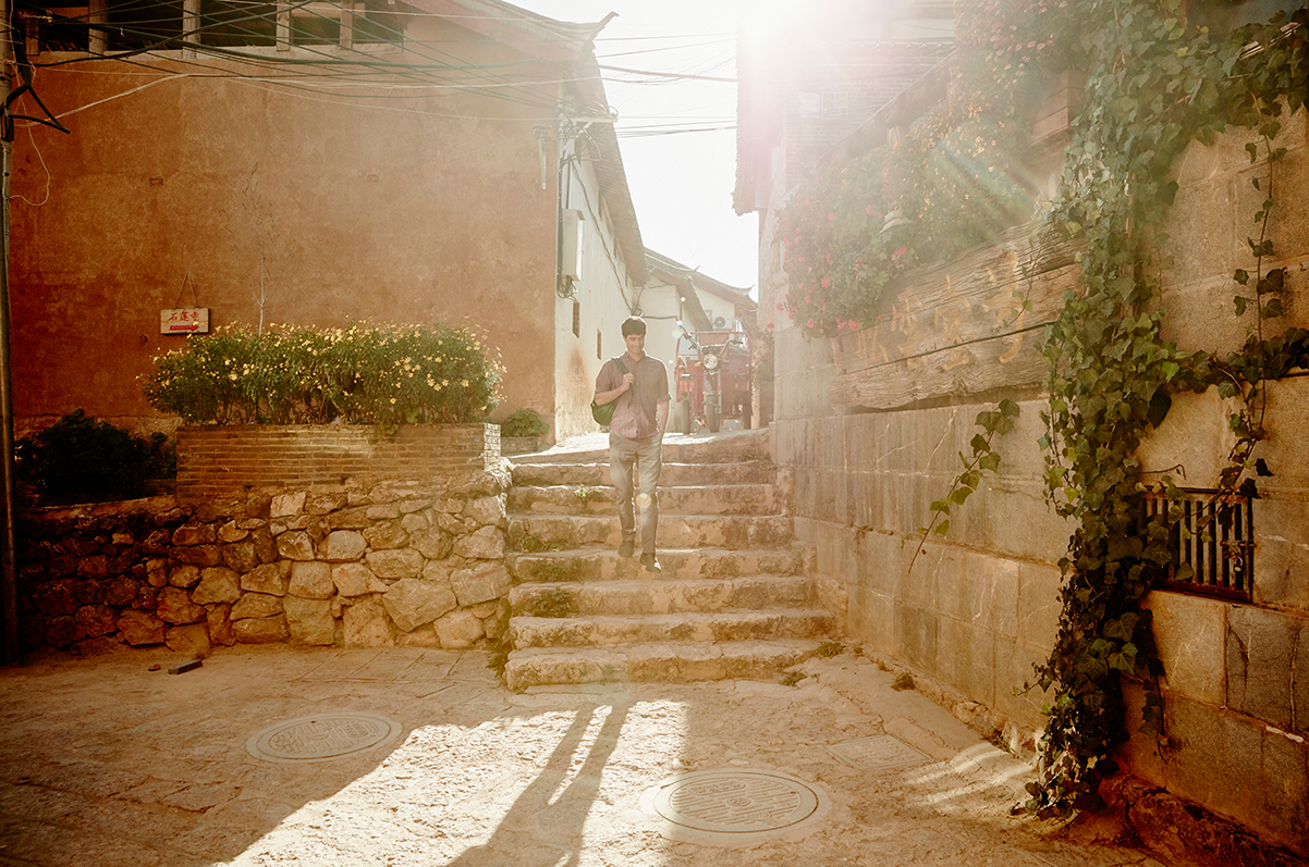 A man wearing a backpack walks down a stone staircase on a warm day.