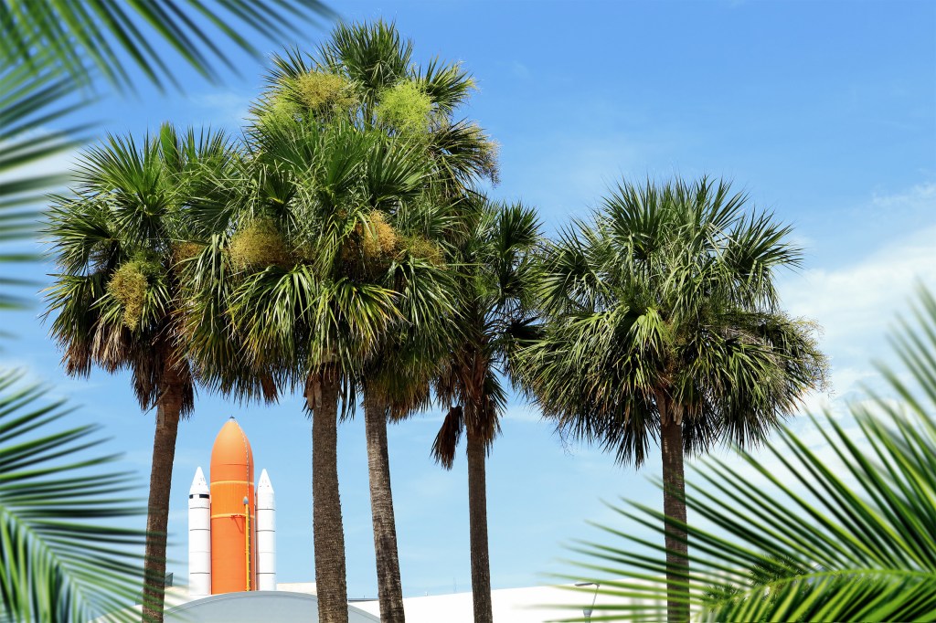 Kennedy space center entrance with space rocket and palm trees over blue sky in Cape Canaveral Florida, USA.