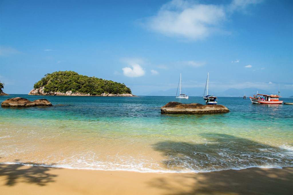A beach on a sunny day with boats in the water in Ubatuba, Brazil.