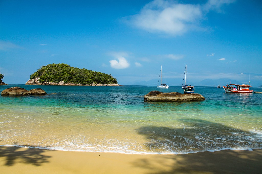 A beach on a sunny day with boats in the water in Ubatuba, Brazil.