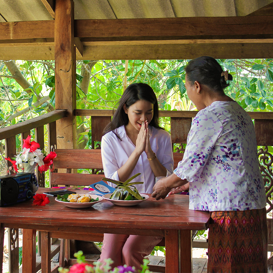 A young woman bows with gratitude as her host places a delicious meal on the table in front of her in Buriram, Thailand.