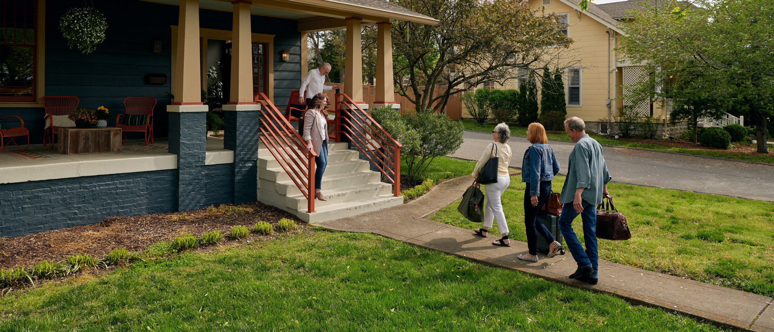 An Airbnb host couple welcome three adult guests at their front porch.