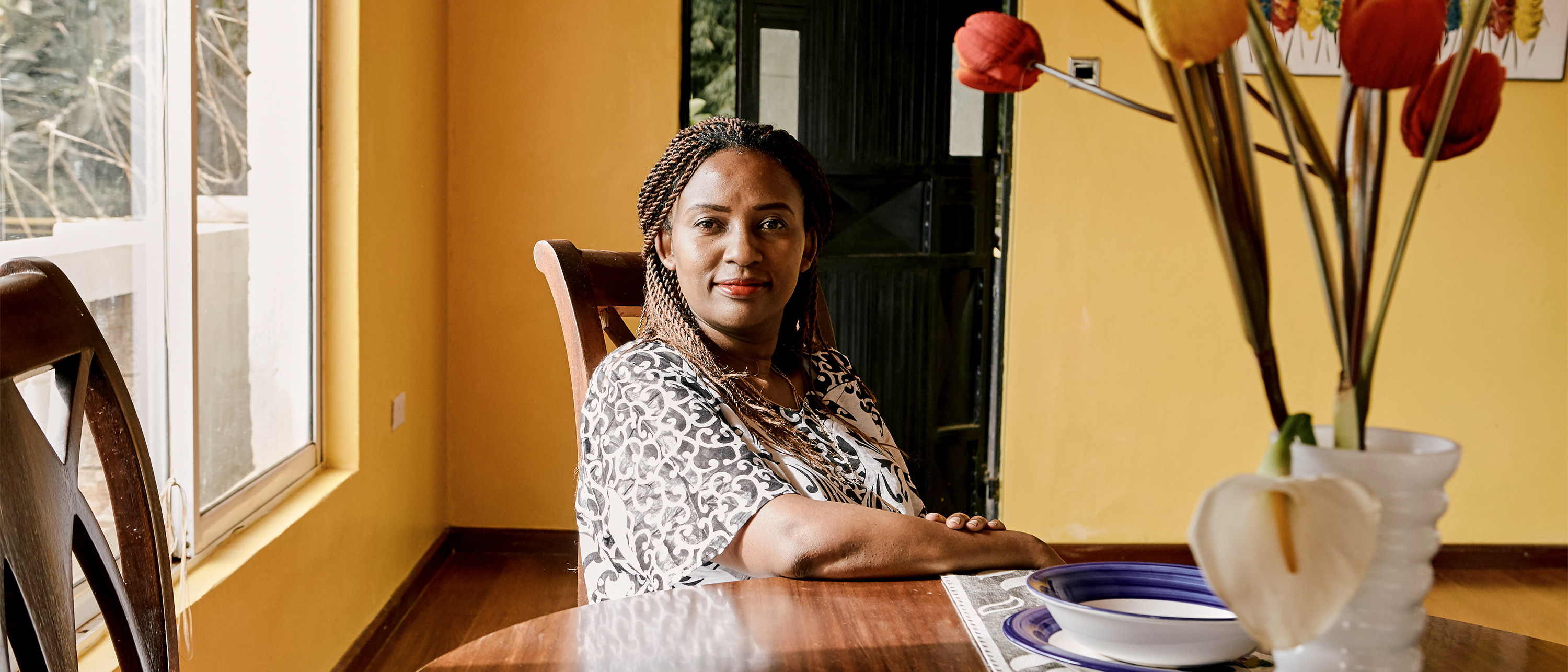 A welcoming Airbnb host sits at her dining room table during a sunny day.