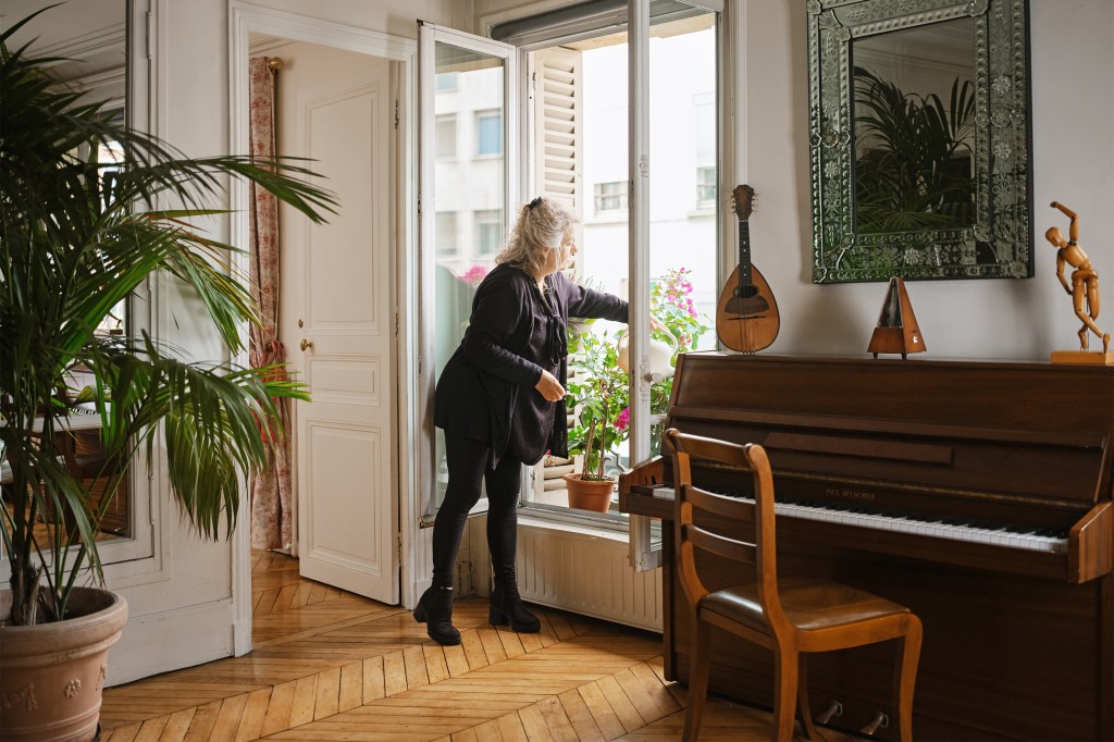 An Airbnb host waters blooming plants outside her window next to a piano.