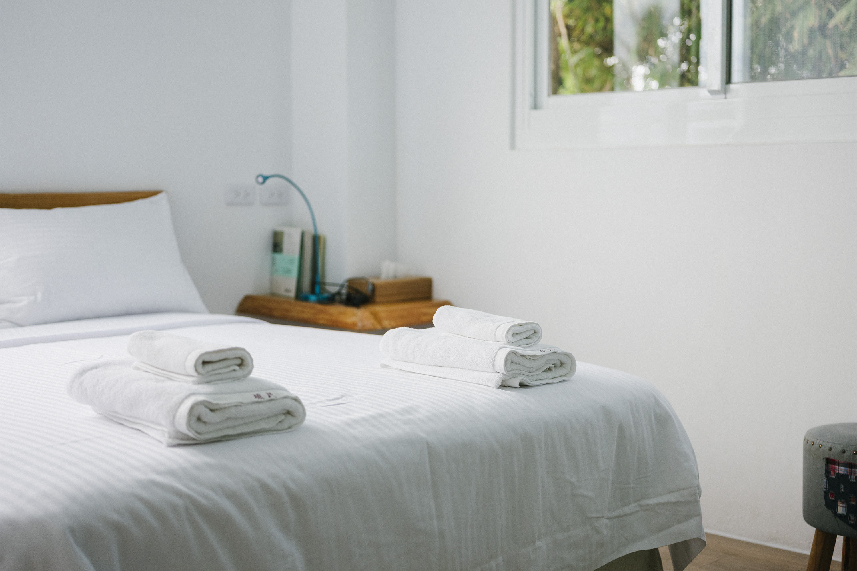Two sets of clean towels rest at the end of a white bed in an Airbnb listing.