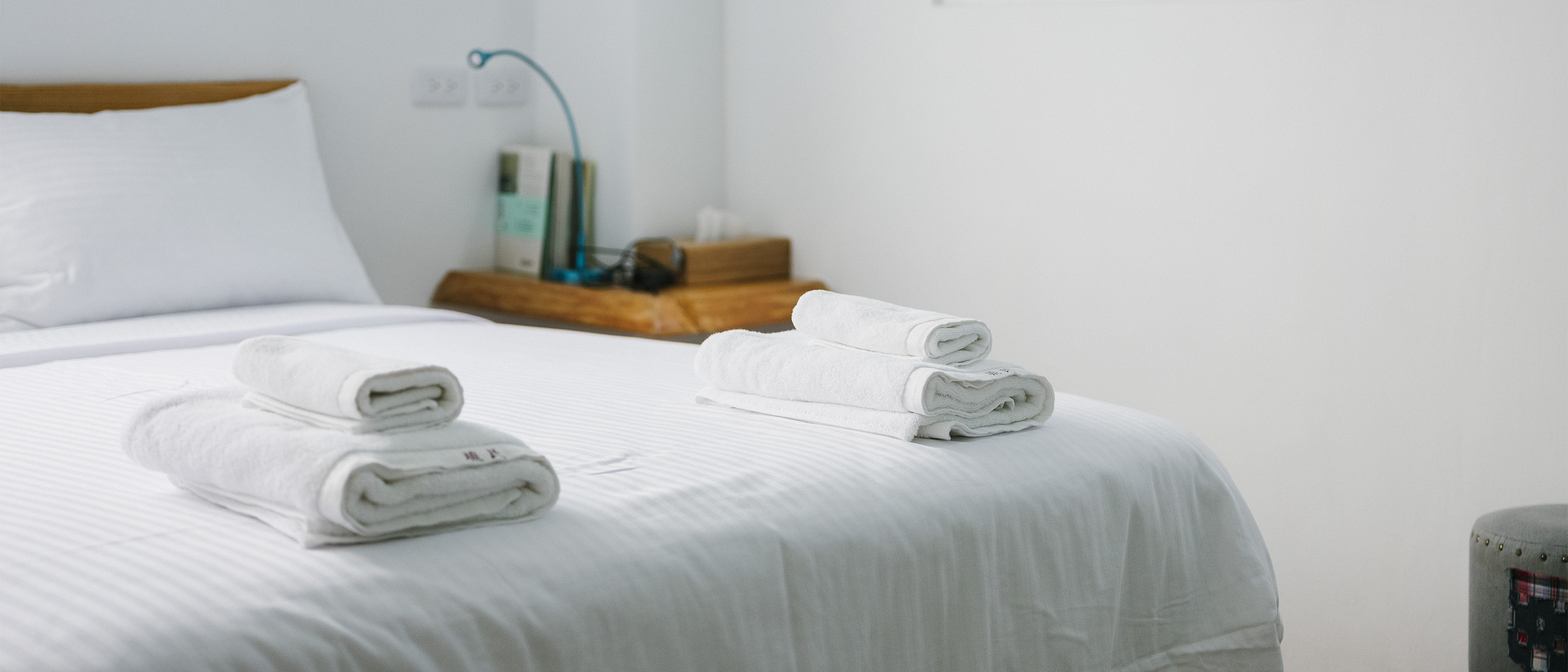 Two sets of clean towels rest at the end of a white bed in an Airbnb listing.