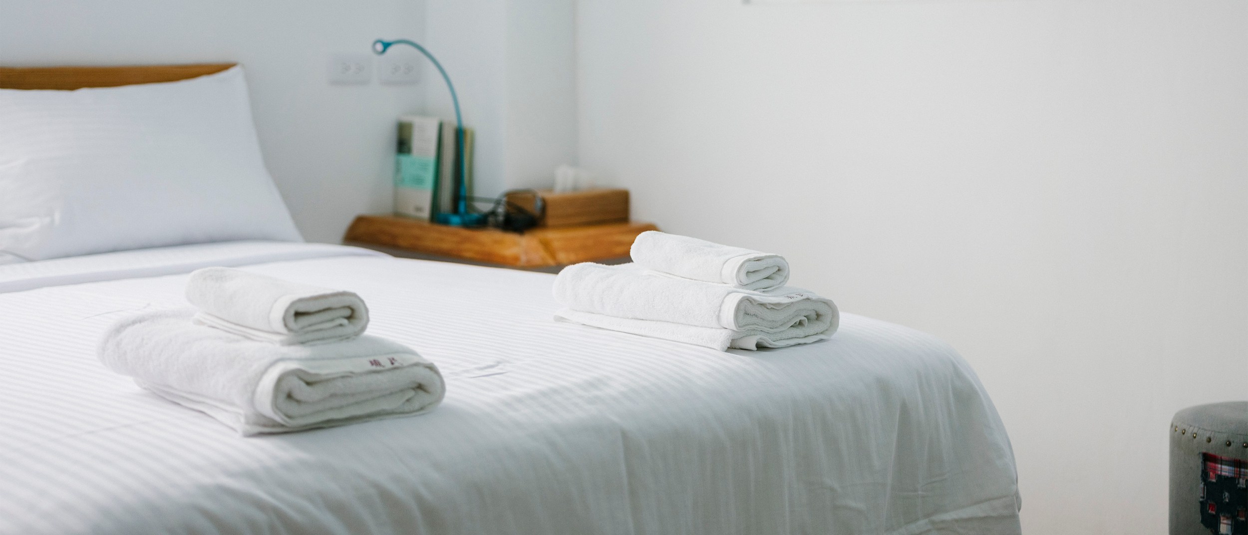 Two sets of clean towels rest at the end of a white bed in an Airbnb listing.