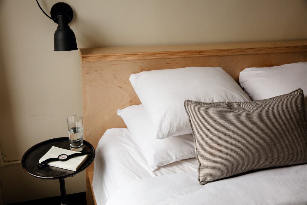 A guests watch rests on a side table next to a clean and comfortable bed in an Airbnb listing.