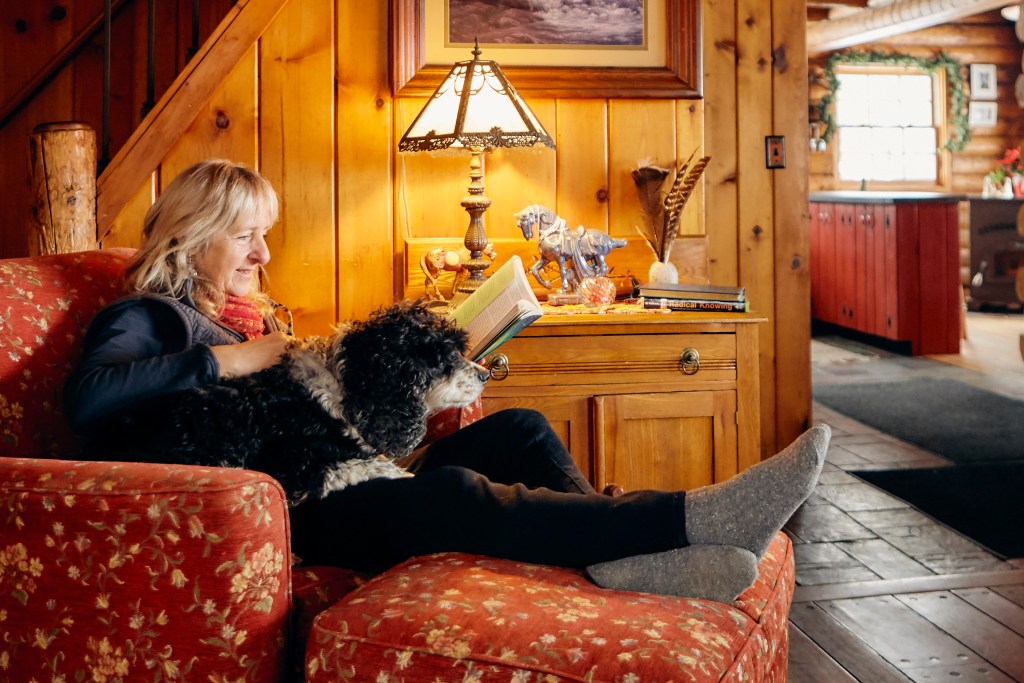 A woman relaxes with her dog while reading a book on a lounge chair in an Airbnb listing.