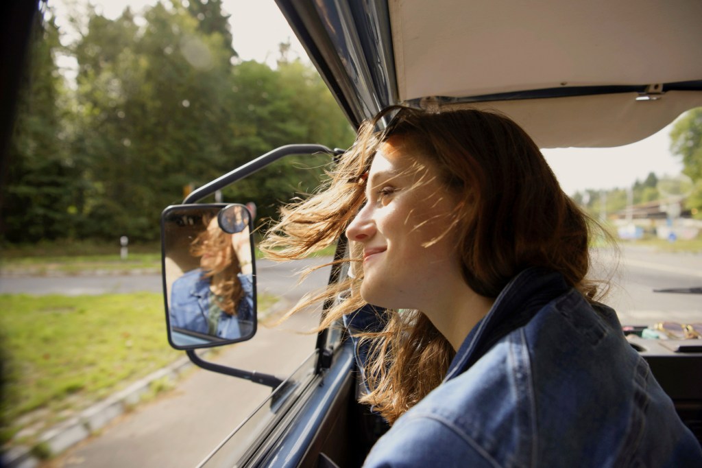 A woman enjoys the nice views and wind in hair while riding on a road trip. 