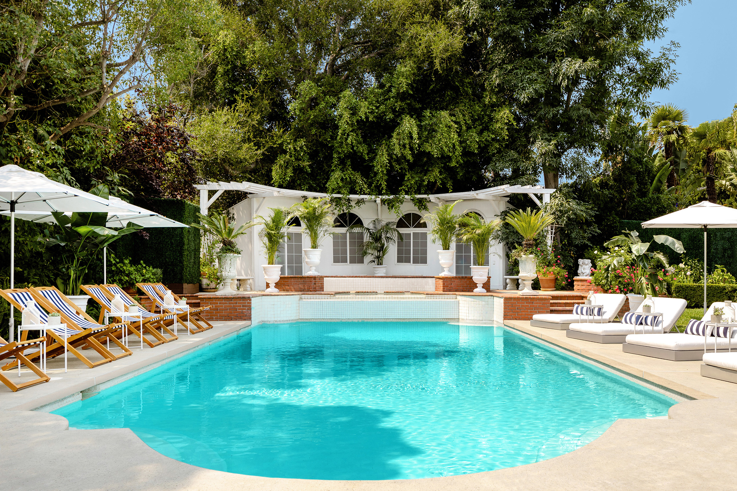 A pool with clear vibrant blue water is surrounded by a lush garden and luxurious lounge chairs.