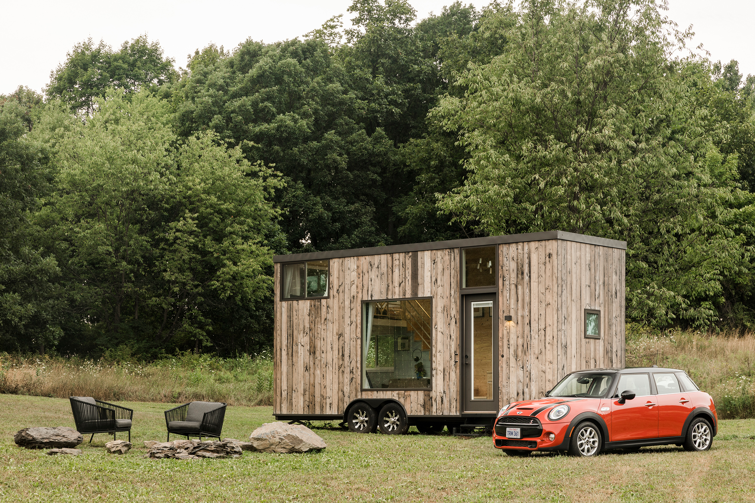 A red MINI Cooper is parked outside of an Airbnb tiny home listing with an outdoor seating area in Marlboro, New York.