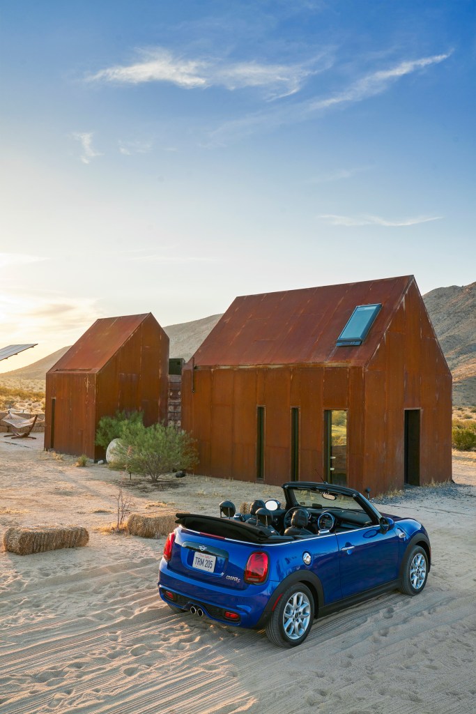 A blue convertible MINI Cooper is parked outside of an Airbnb tiny home listing in the desert of Twentynine Palms, California.