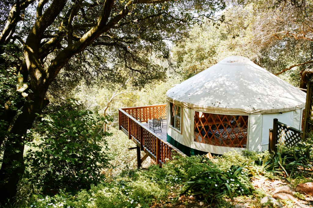 Glamping white canvas yurt with a wraparound balcony situated on a hillside.