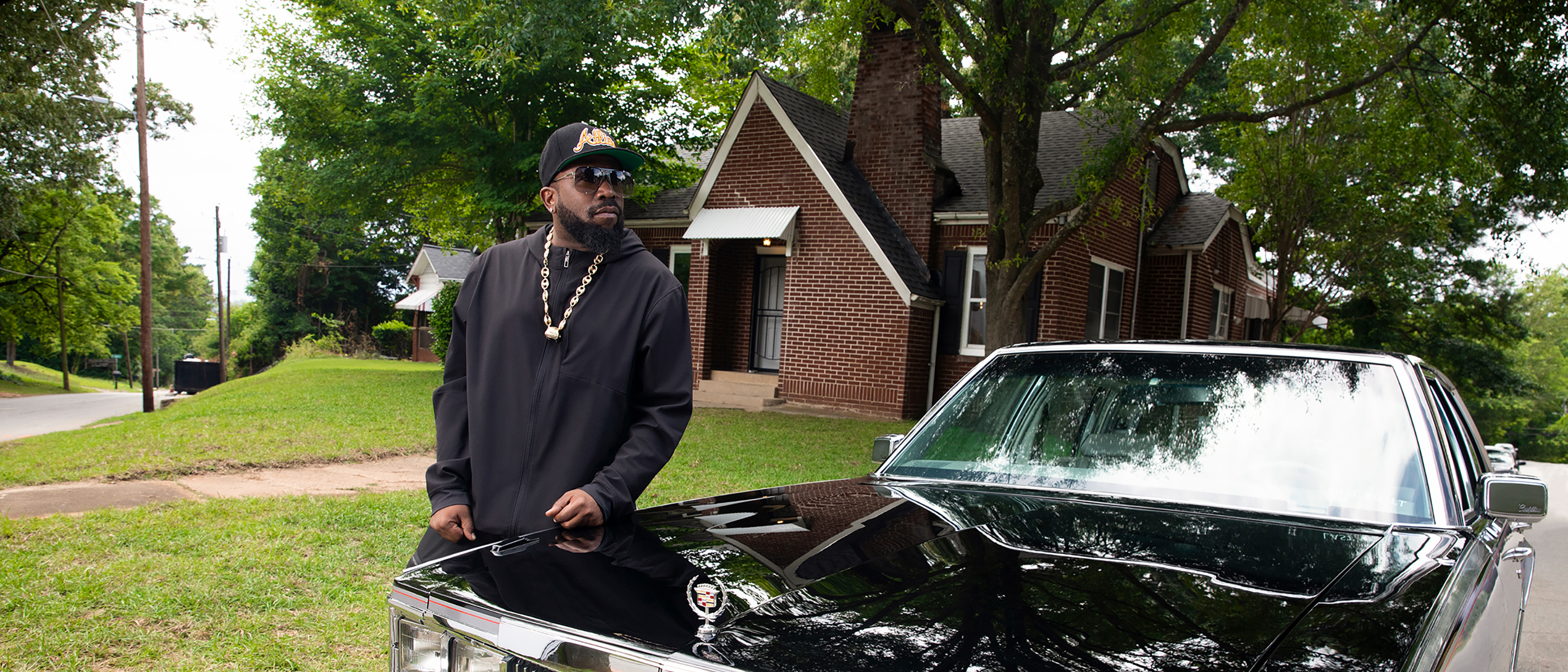 Big Boi standing alongside a vintage Cadillac car parked outside the Dungeon House