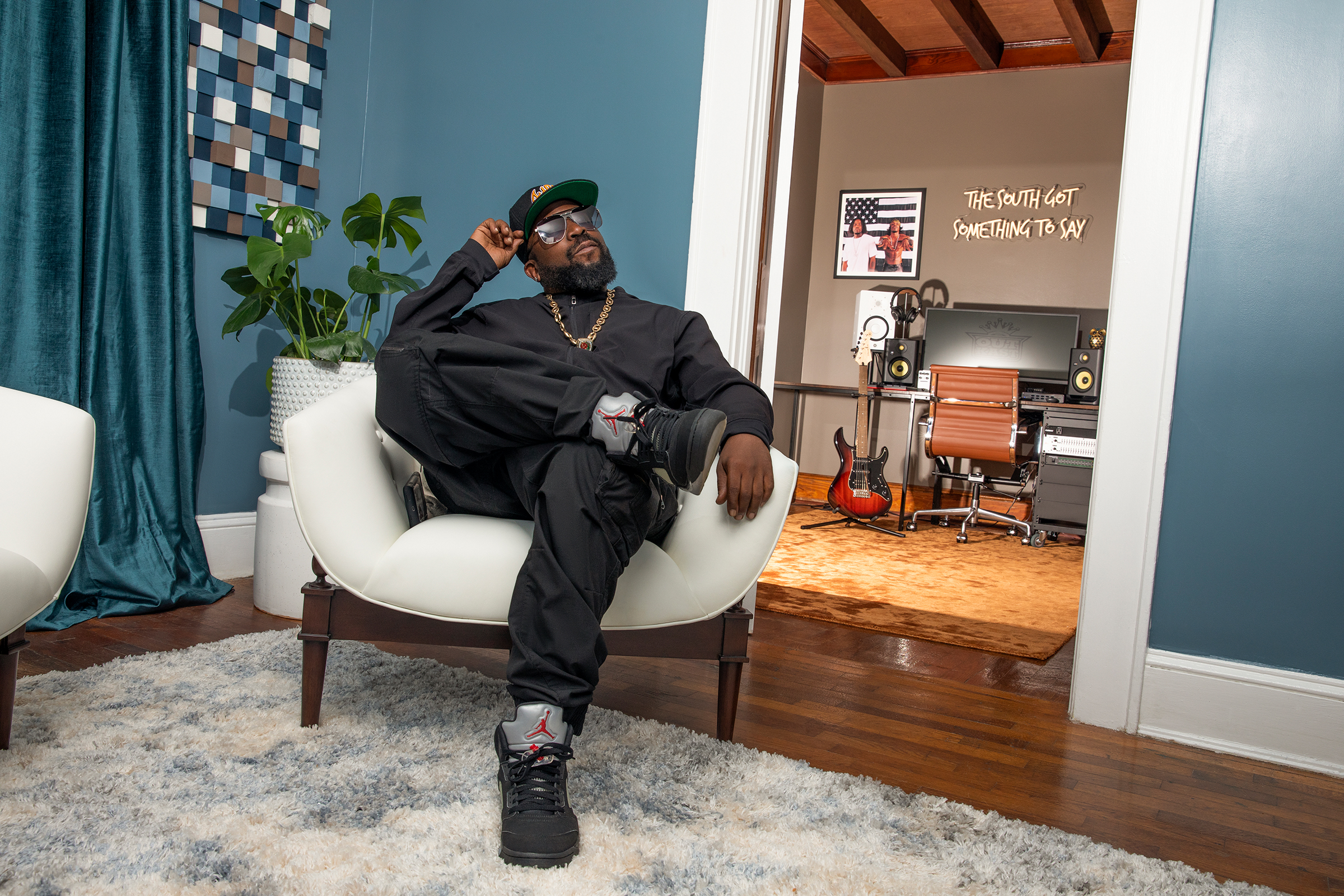 Big Boi sitting in white living room chair with office space in The Dungeon House in the background