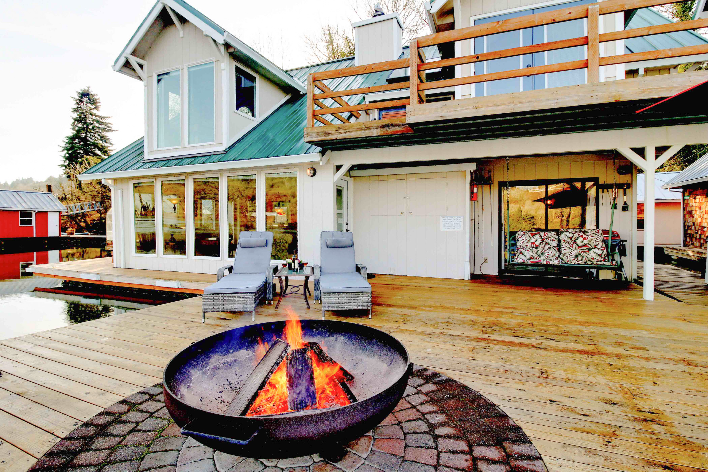 Floating white house with an extended dock and patio crossover with a fire pit in the foreground.