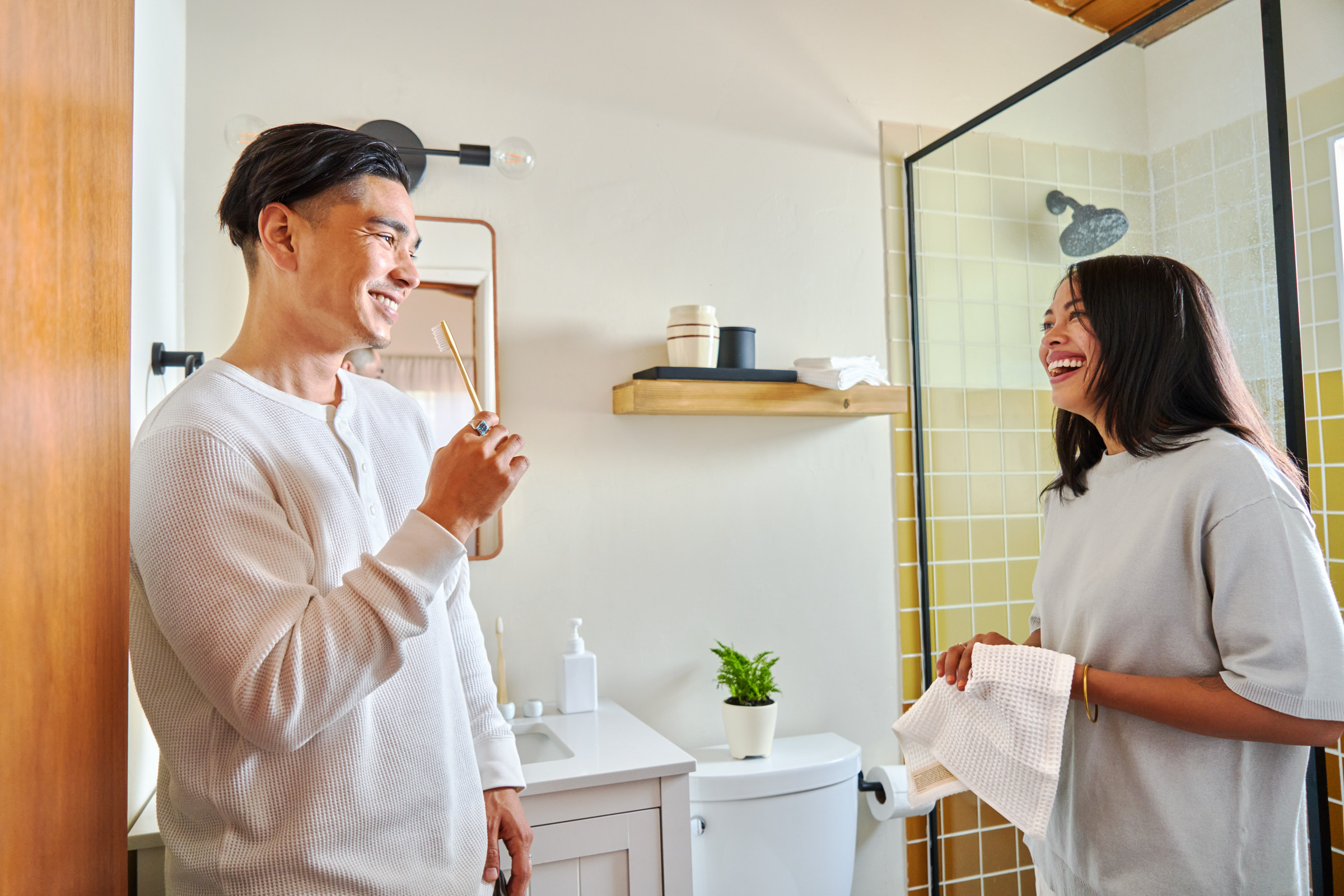 Male and female guest laugh in the bathroom of their Airbnb, holding towel linens featured in the essential kit.