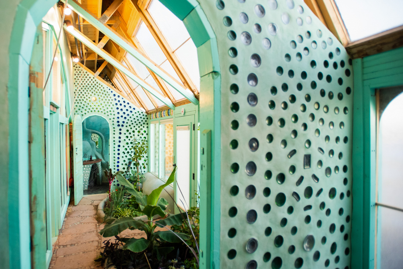 Long hallway view of earthship house with green walls constructed of green earthen material and recycled bottles.