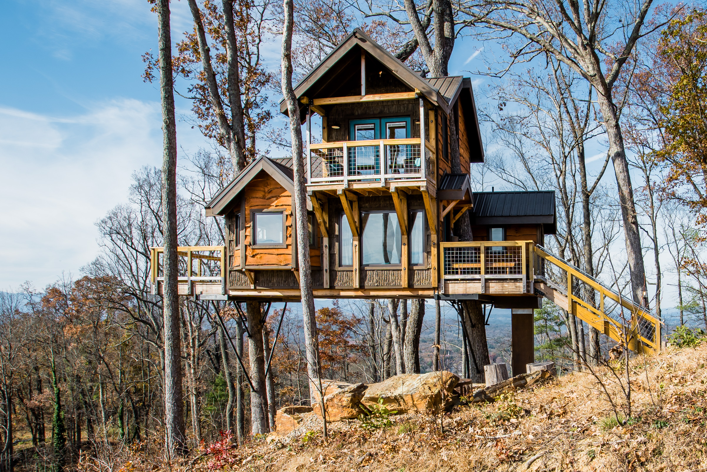 Modern treehouse with three wings elevated amongst bare trees on a hillside.