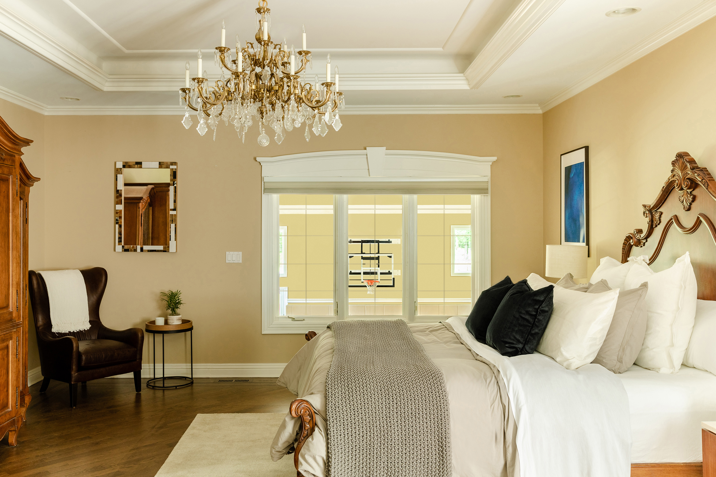 The bedroom features an elaborate chandelier, large comfortable bed, and windows that overlook the indoor basketball court.
