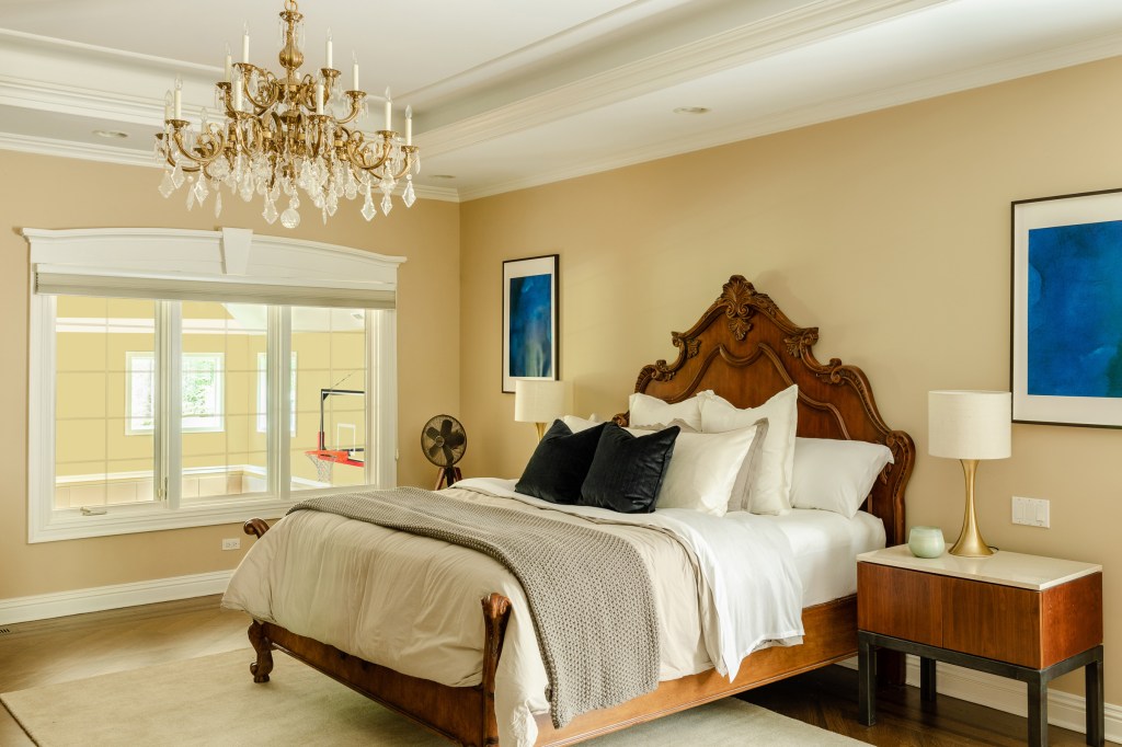The bedroom features an elaborate chandelier, large comfortable bed, and windows that overlook the indoor basketball court.