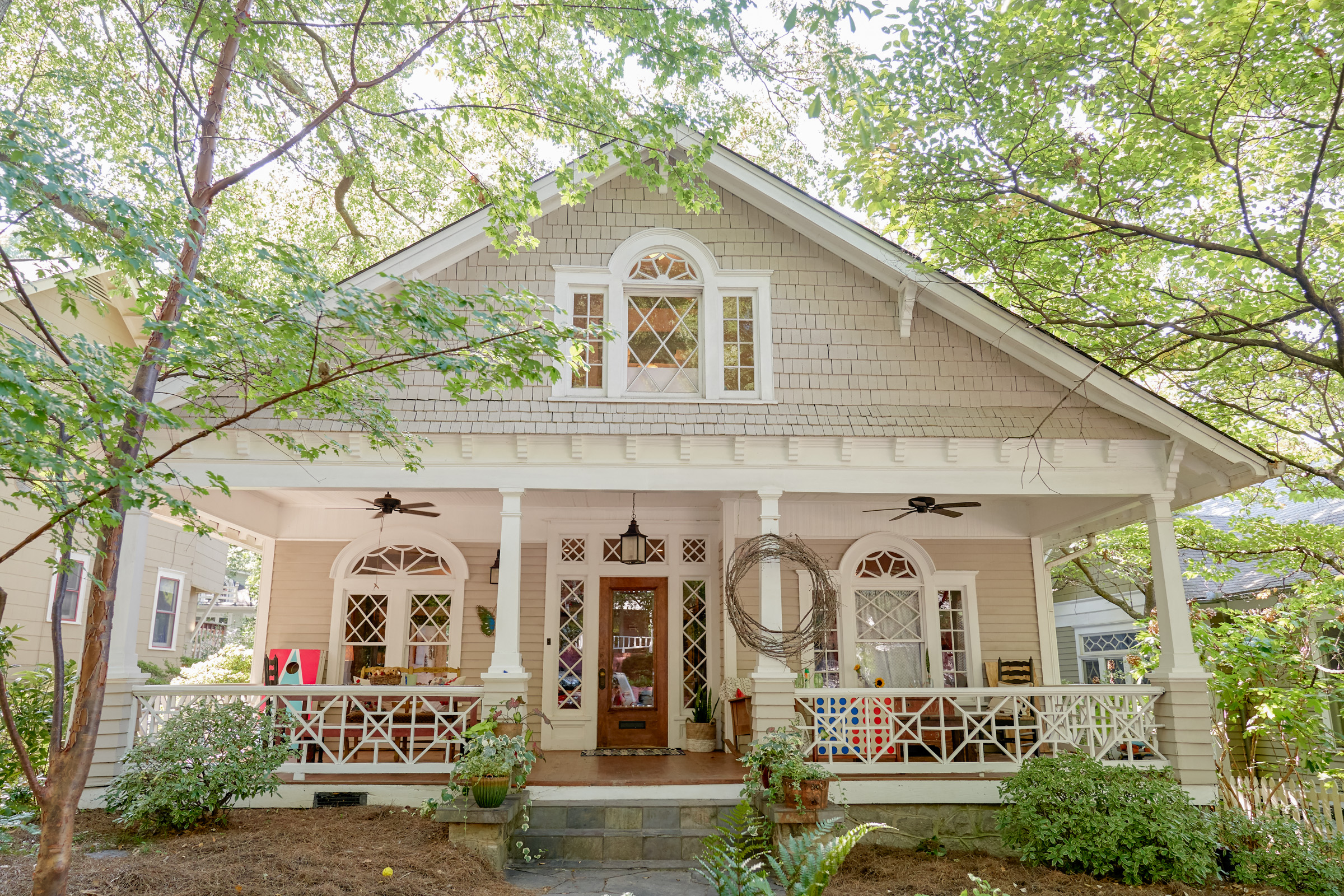 Charming white house with a front porch surrounded by green trees.
