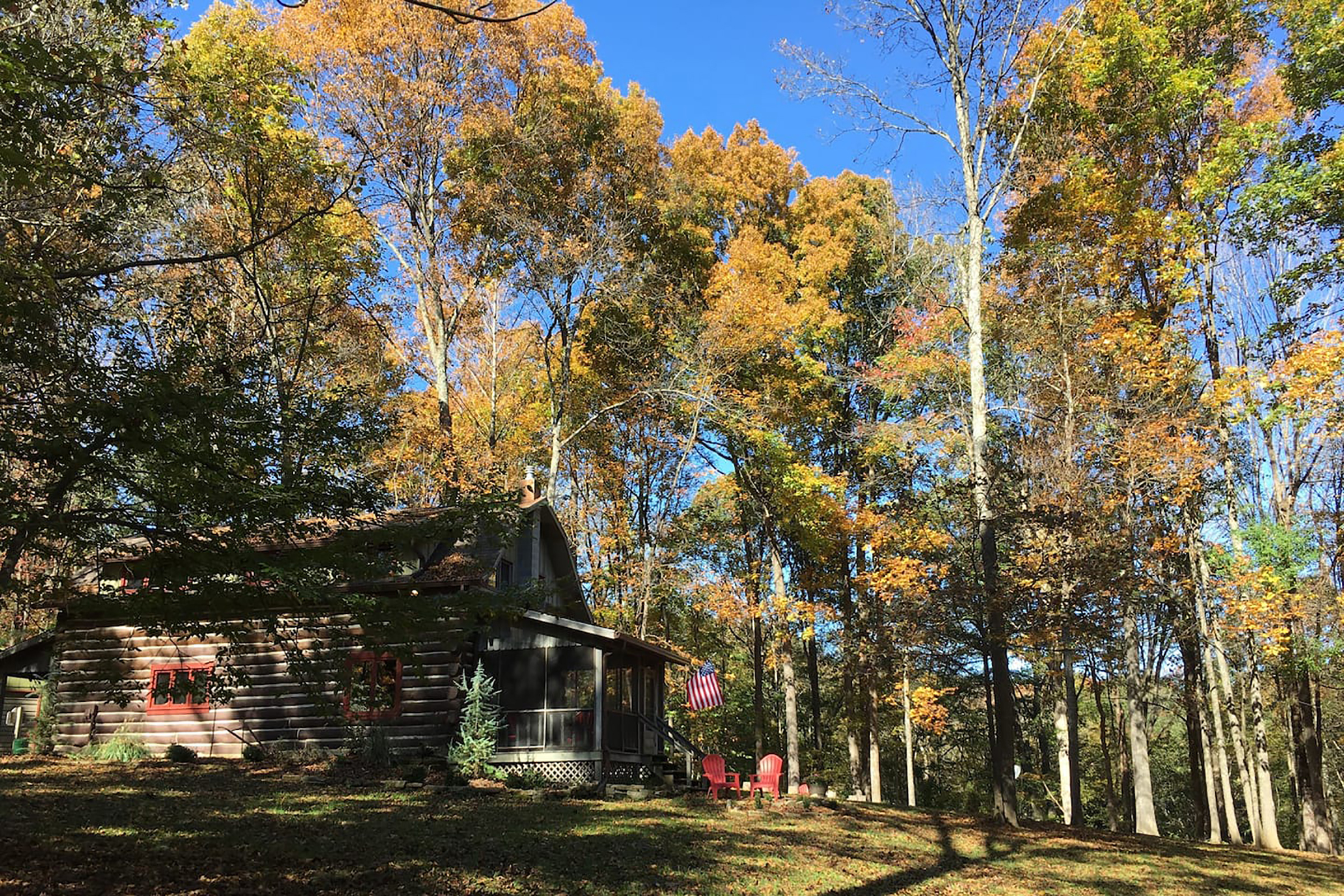 A cabin with an American flag hanging out front and red lounge chairs in the yard.