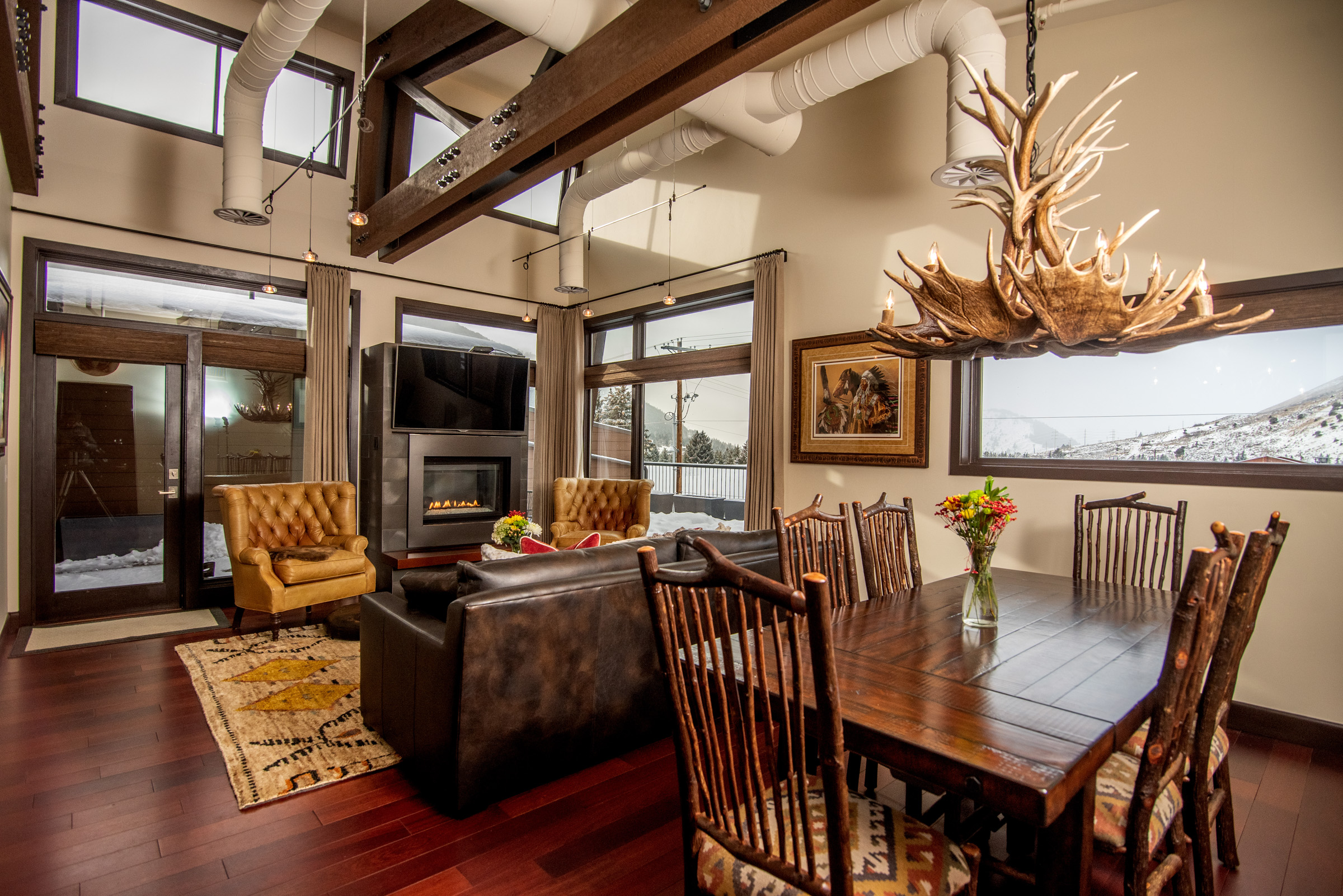 Lodge themed living room shot with dining table in foreground and antler chandelier with living room seating area in the background.