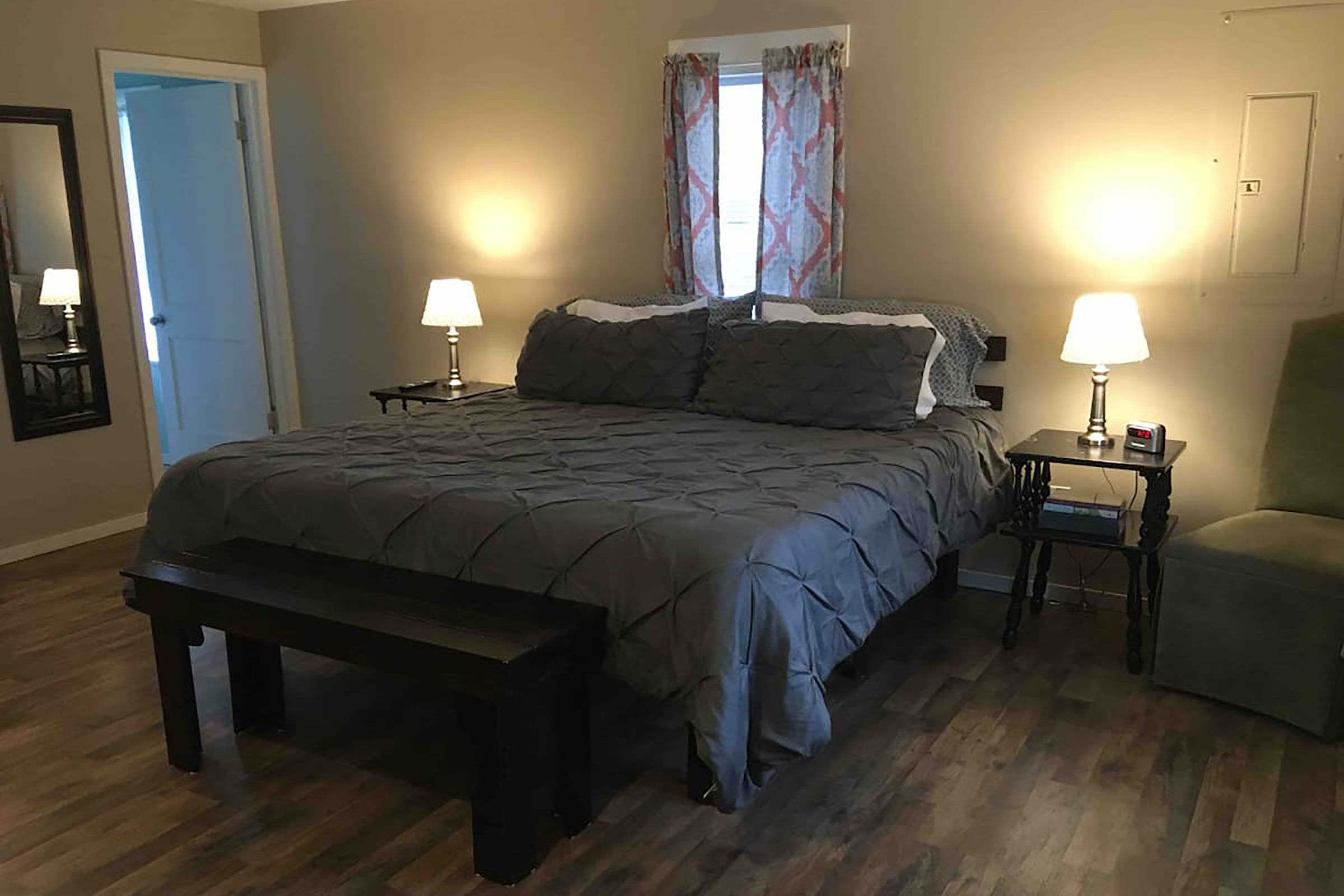 A bed with a dark comforter in between two night stands with illuminated lamps on both ends.