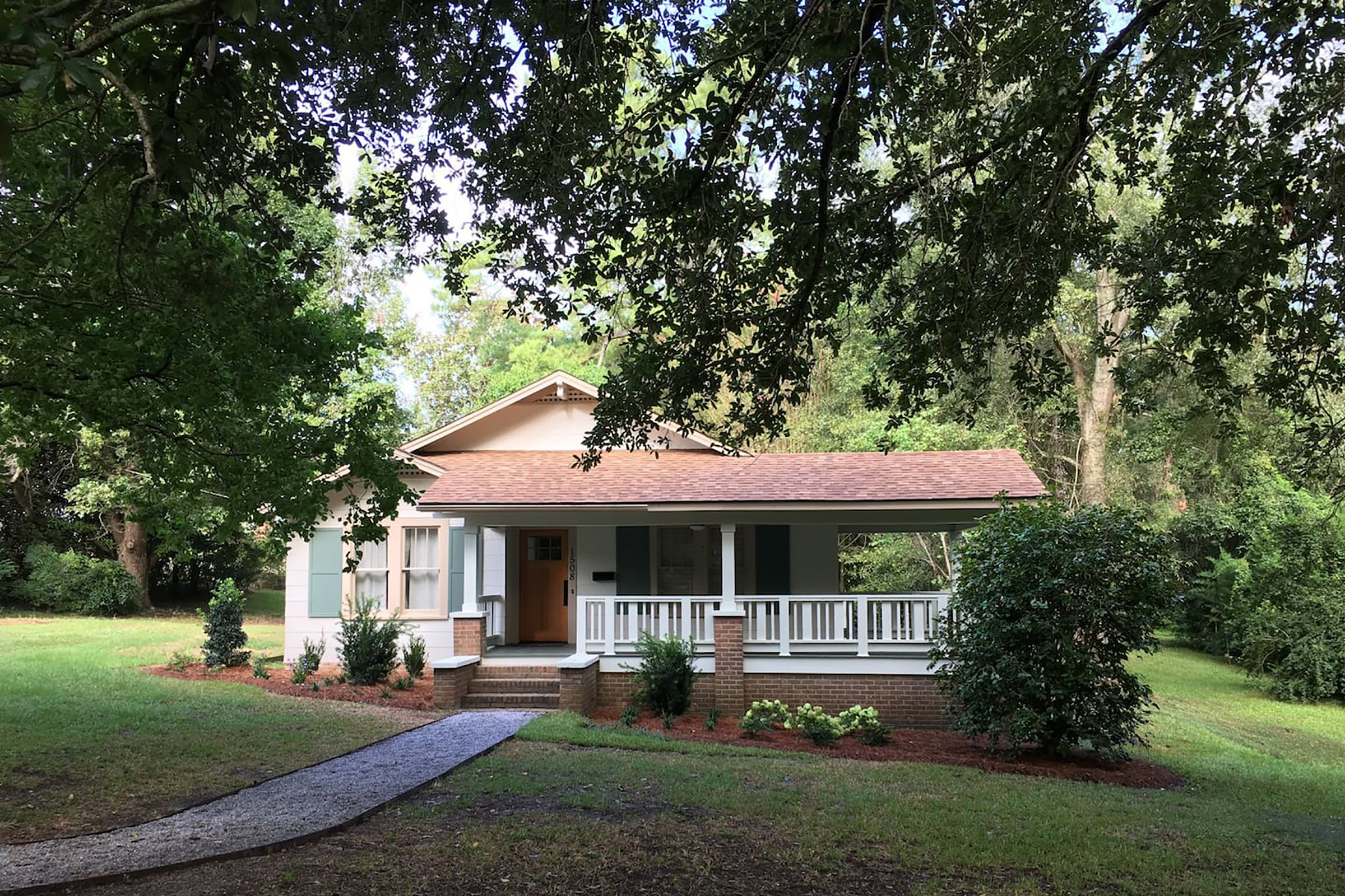 A cream colored ranch home with a wrap around front porch and large yard.