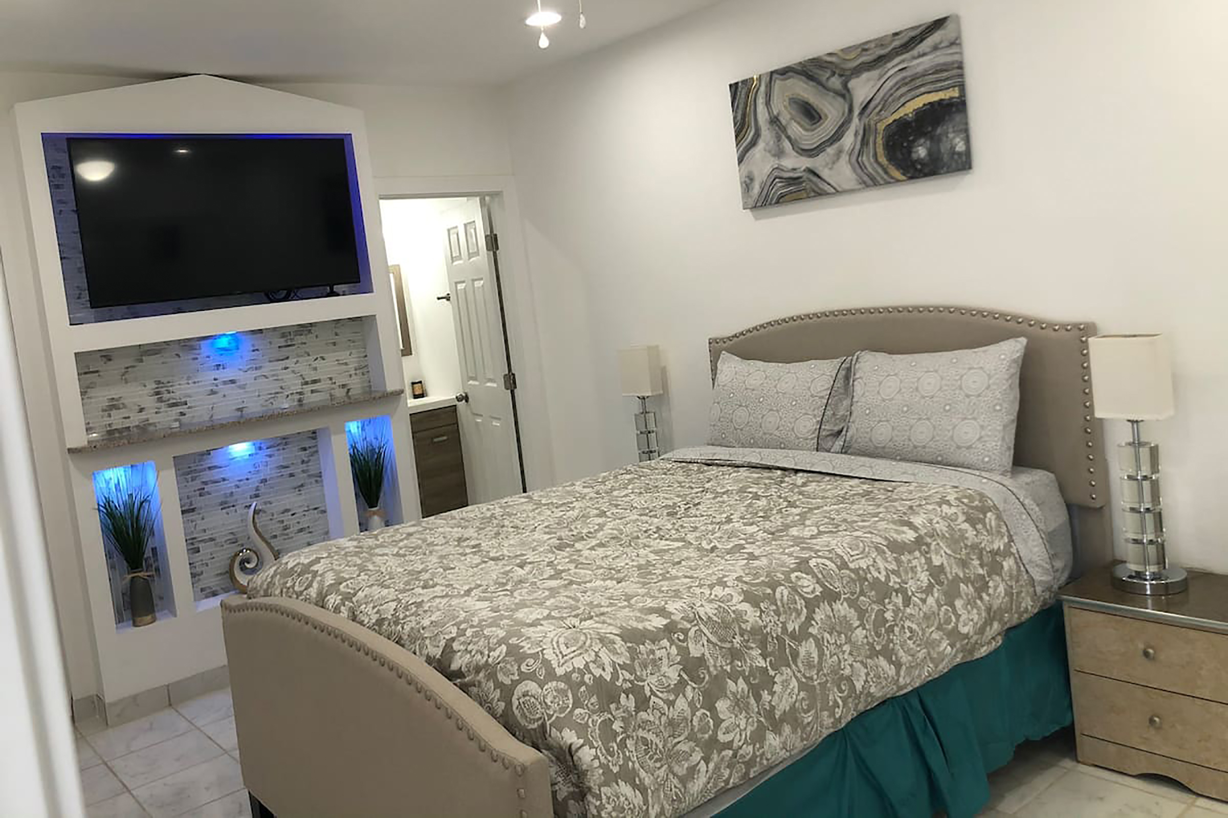 A bed with a floral comforter next to a mounted television with blue backlights.