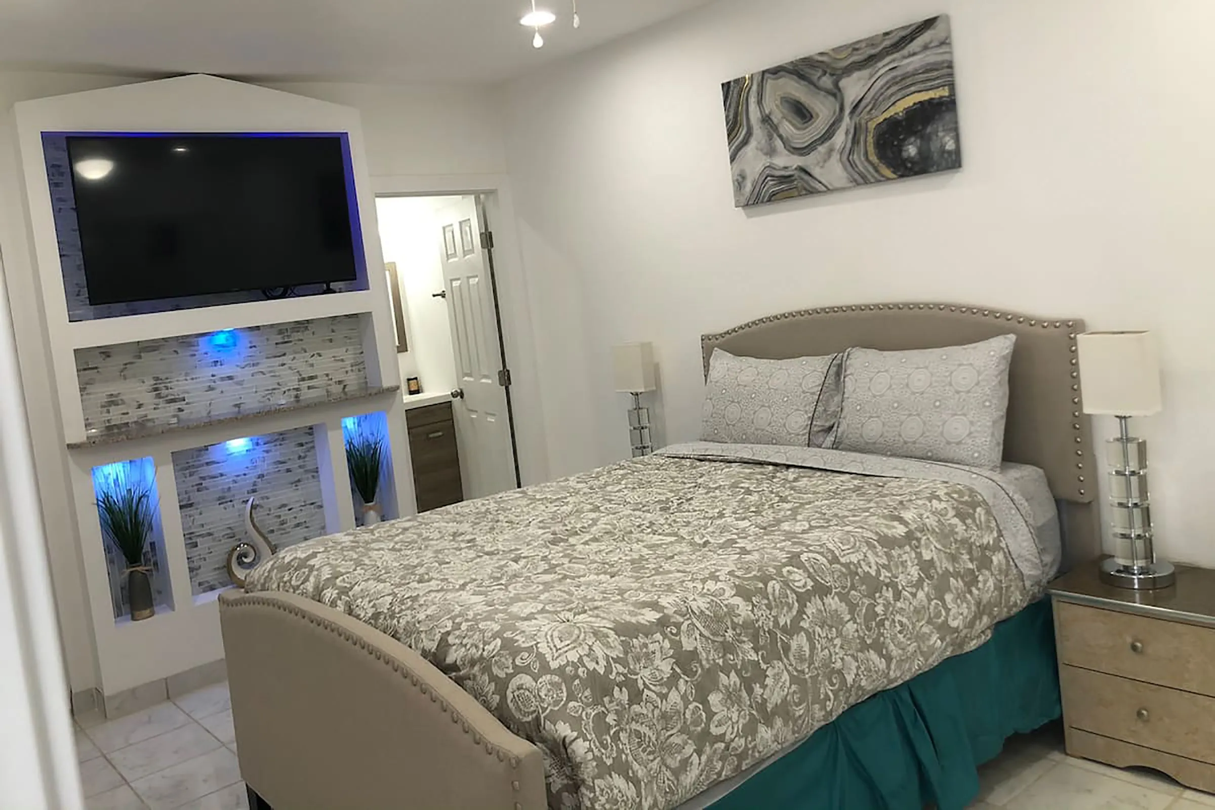 A bed with a floral comforter next to a mounted television with blue backlights. 