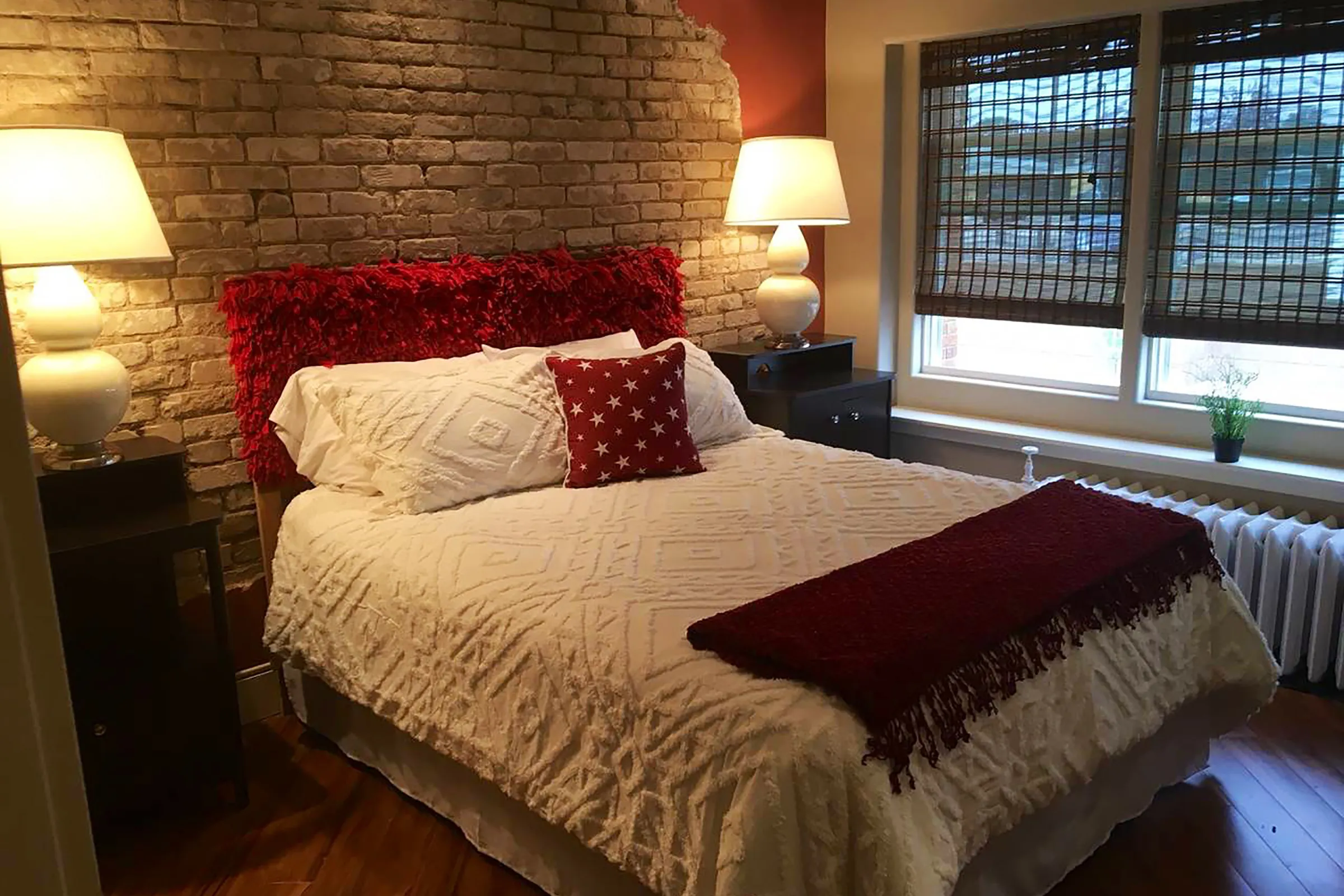 A bed with a white comforter and red throw blanket, with two end tables with light lamps. 