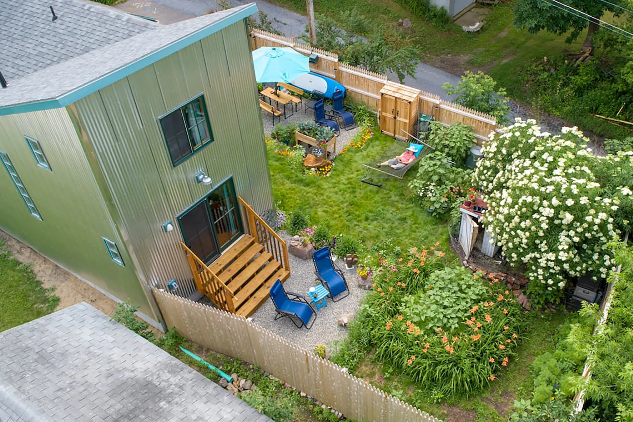 An arial photograph of the backyard of a green house with a lush garden and blue lounge chairs