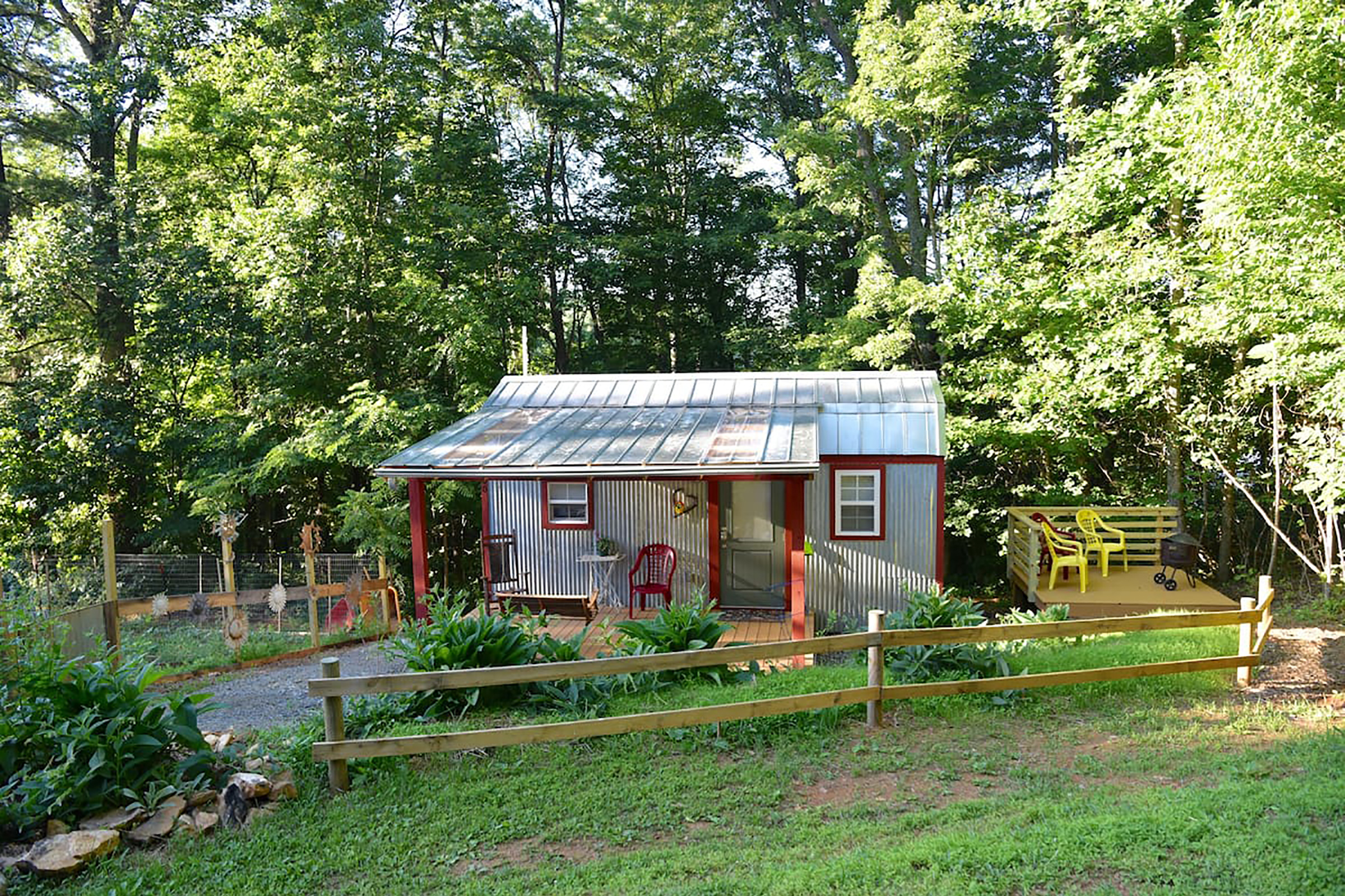 A home with aluminum siding and a large front yard with a patio next to the home with yellow chairs.