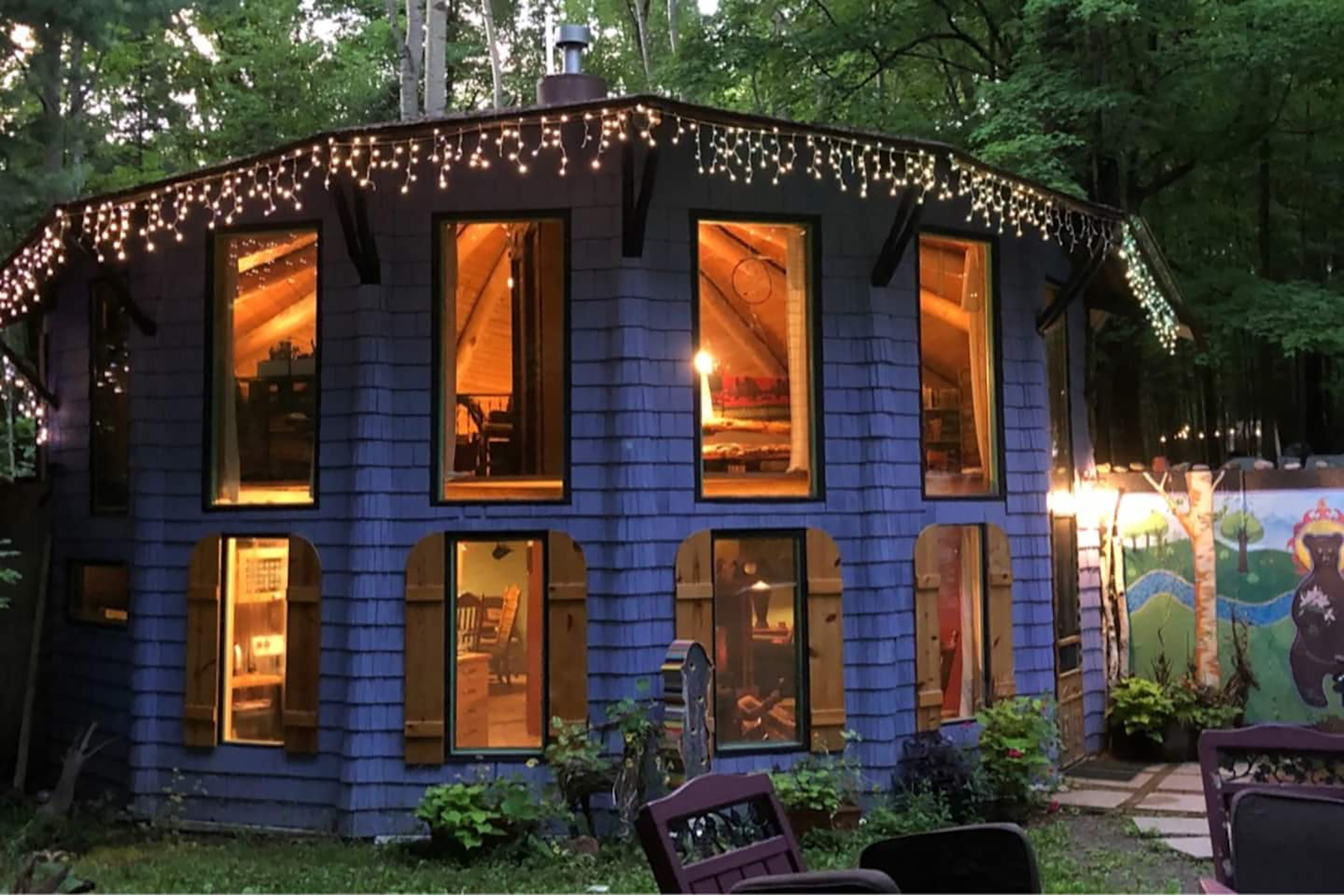 A shingle-sided home with large windows and string lights hanging from the roof. 