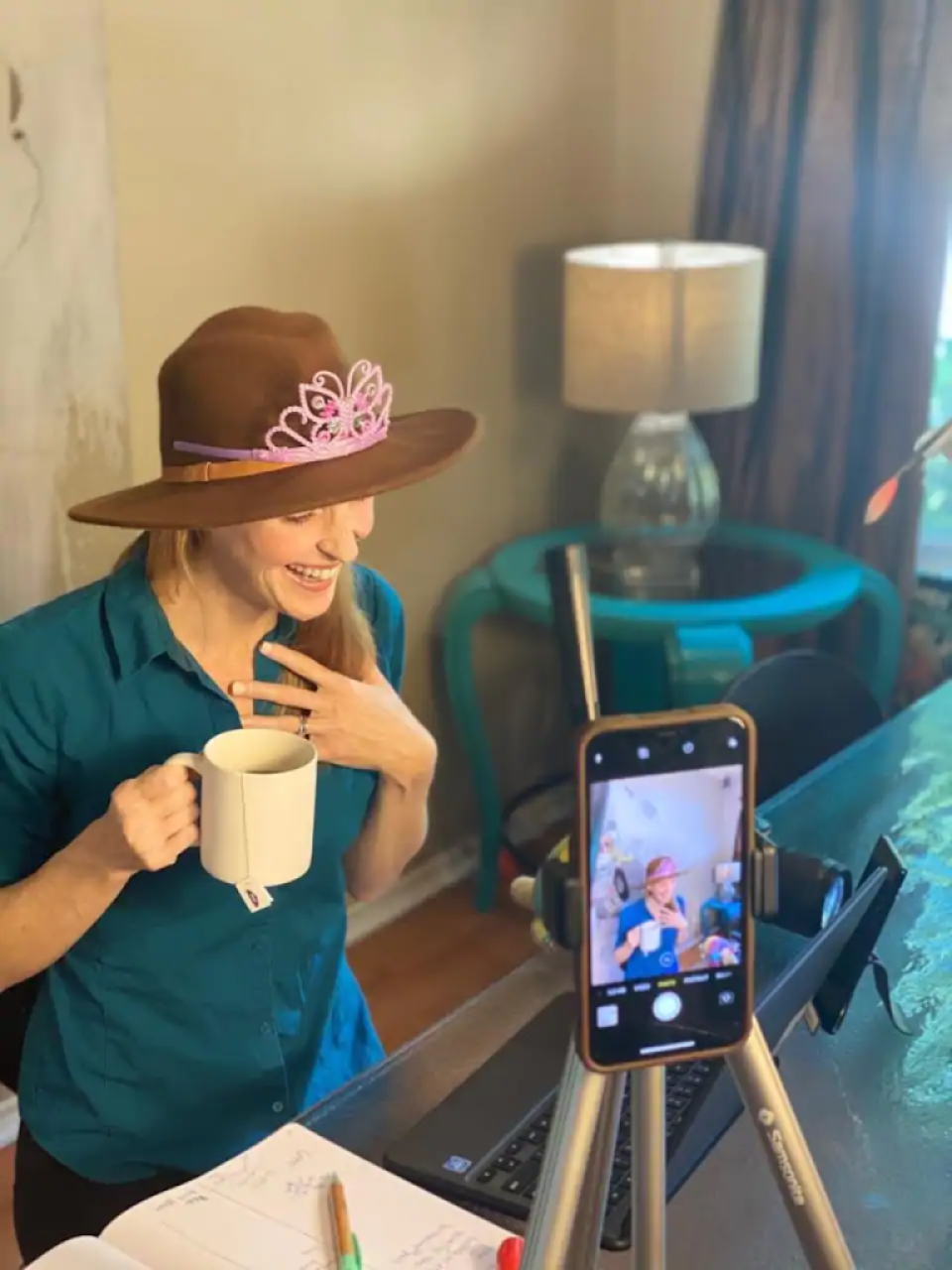 Woman wearing a cowboy hat and a tiara, holding a mug while smiling