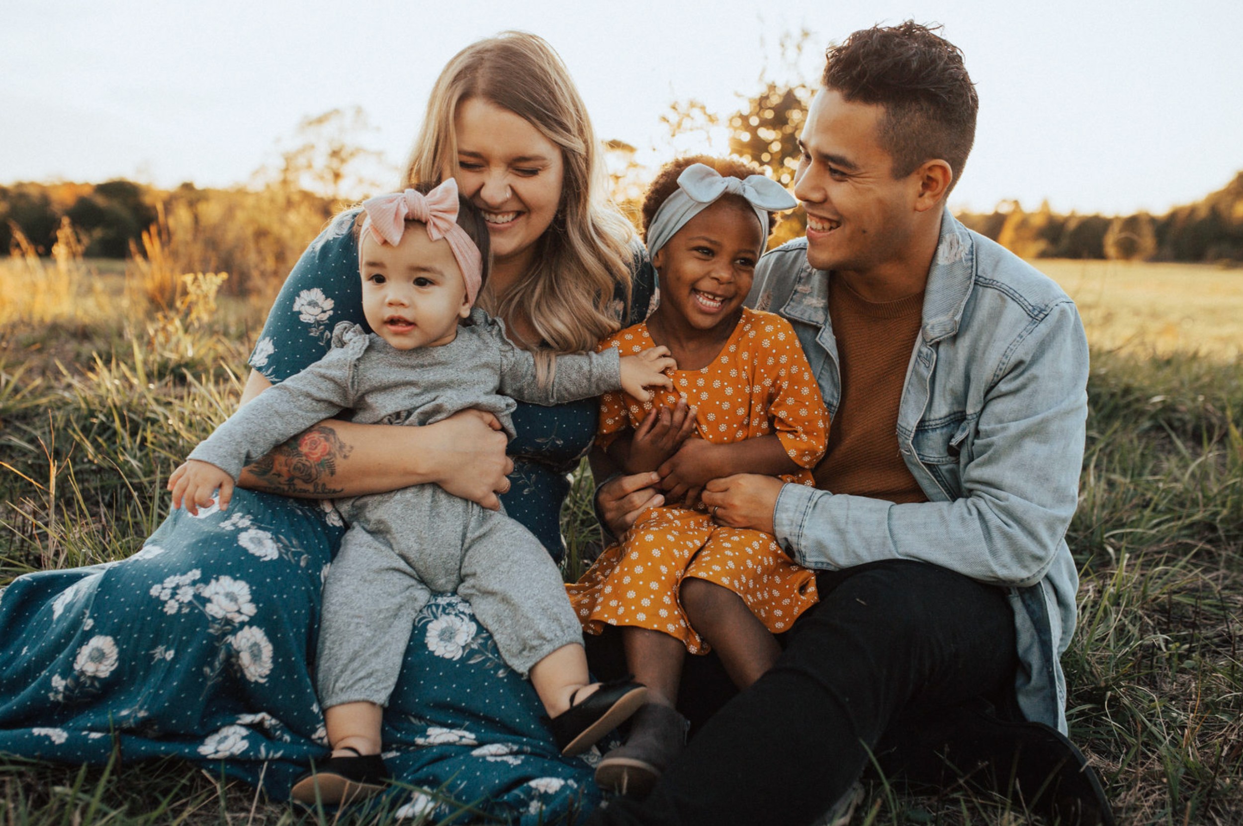 Colin and Meg hugging their two daughters while seated in the middle of a field.