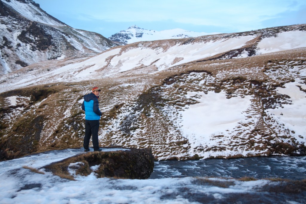 Hendric standing off in the distance on top of rock with a snowy, mountainous landscape behind him.