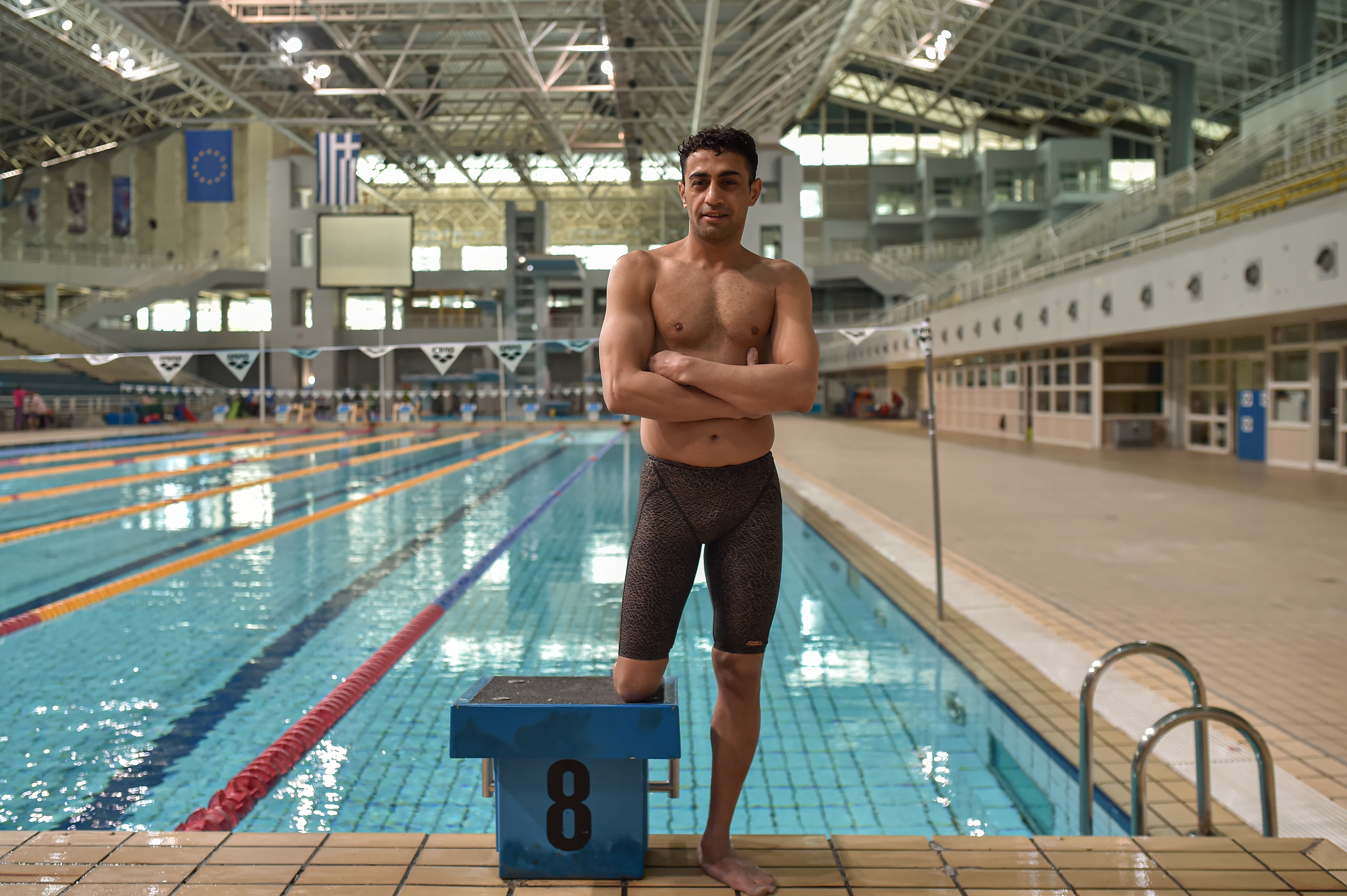 Ibrahim standing facing the camera with arms crossed in front of an olympic sized swimming pool. 