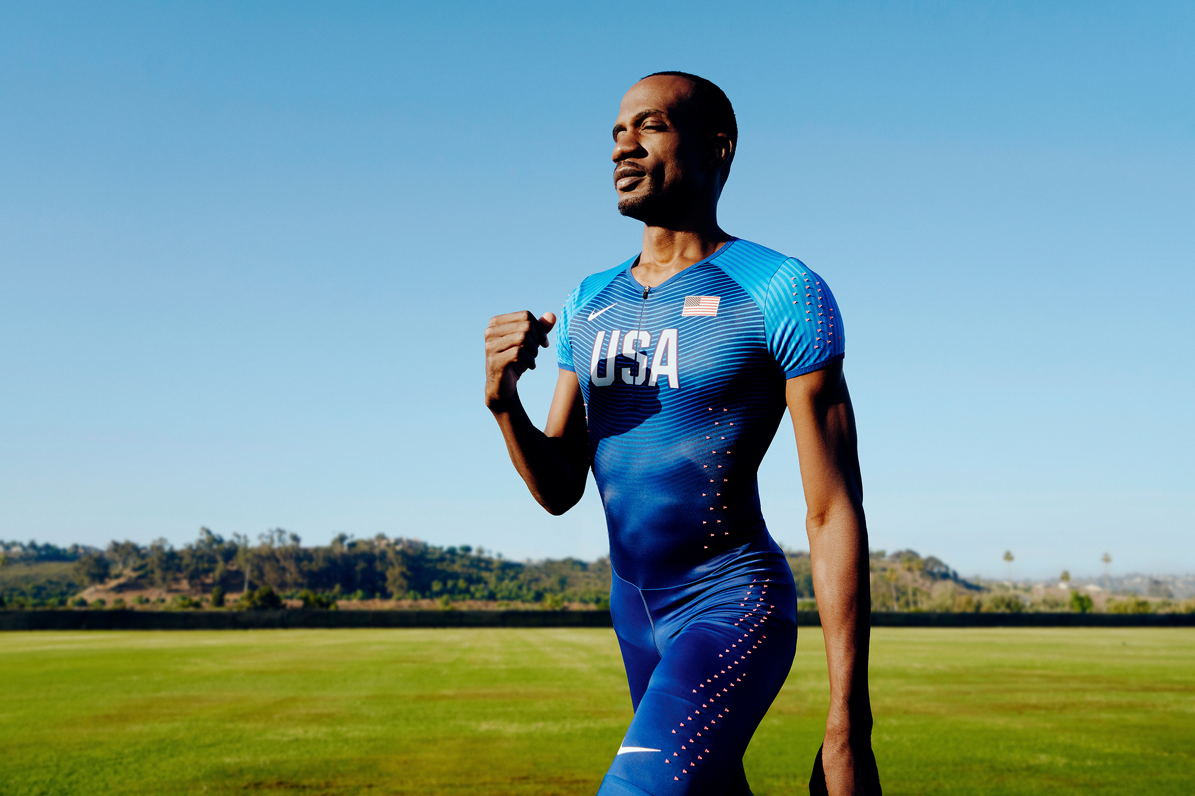 Lex Gillette walking on a track loop wearing an all blue track outfit and a green field behind him.