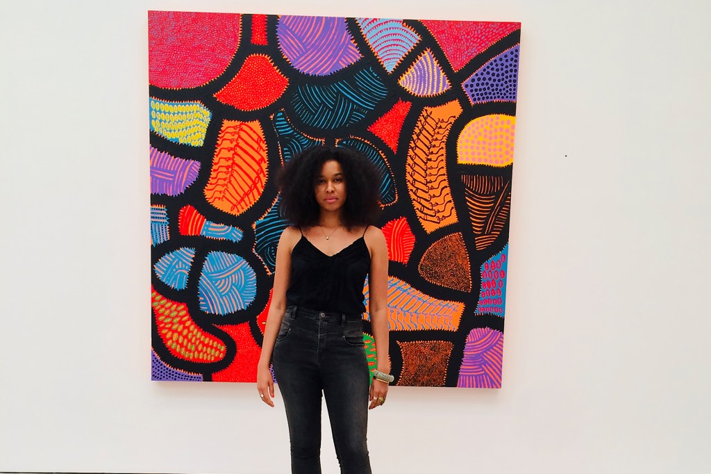 Marquita dressed in black standing in front of a colorful piece of artwork.