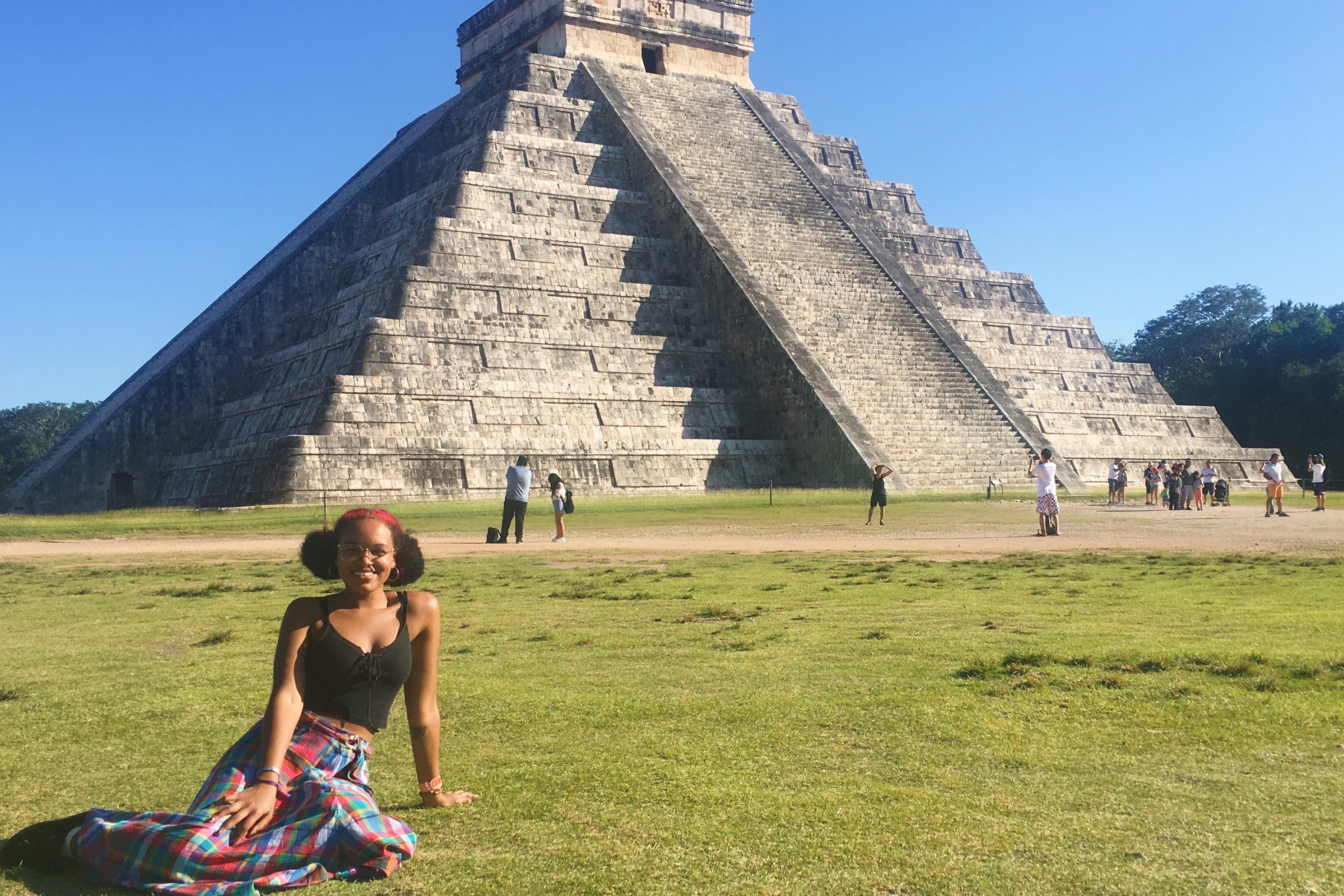 Veronica sits in the grass in the foreground with a pyramid behind her.