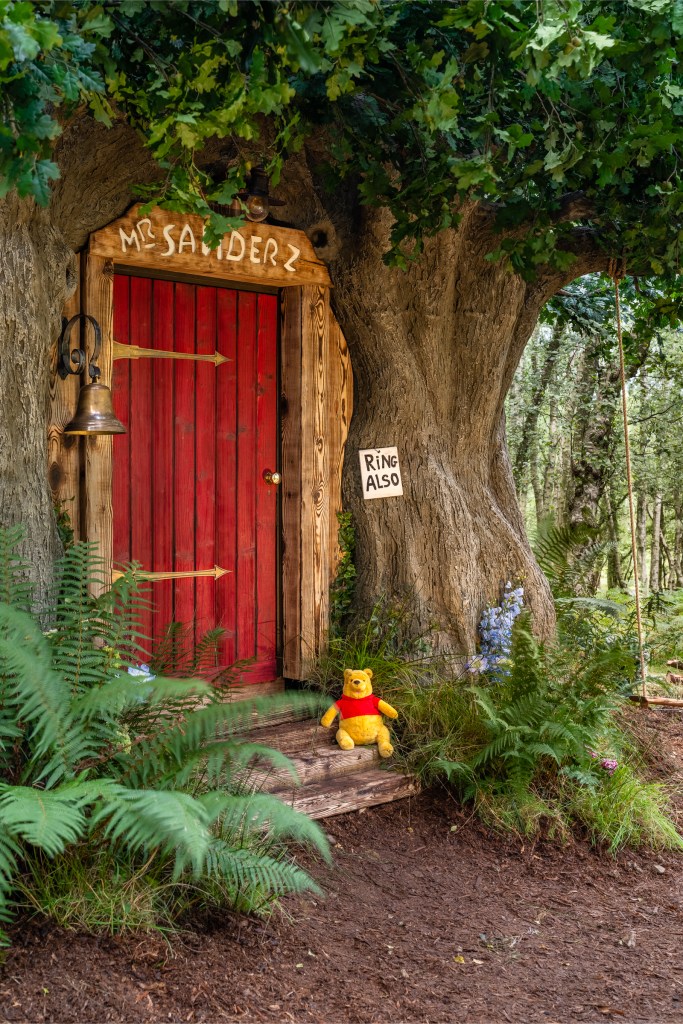 A Pooh teddy sitting on the doorstep to the Bearbnb.